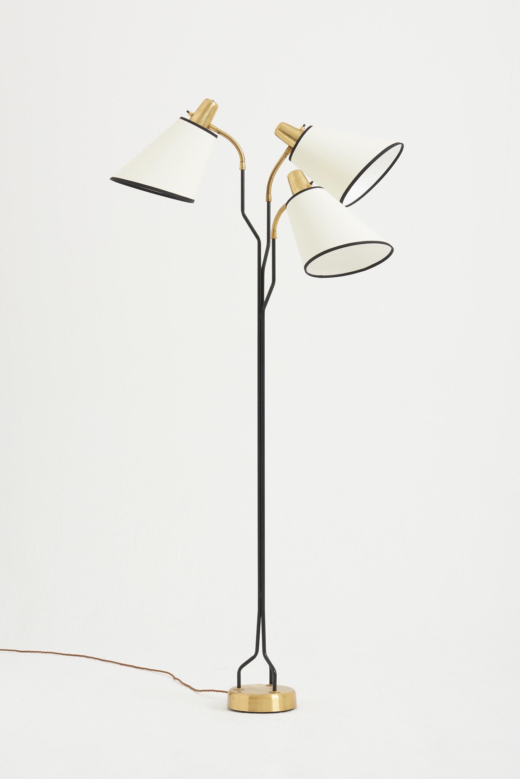 A brass and black enamelled iron three-armed floor lamp.
Sweden, 1950s.
Measures: Overall height:
Diameter of the base: 17 cm 
Diameter of each shade: 22 cm.