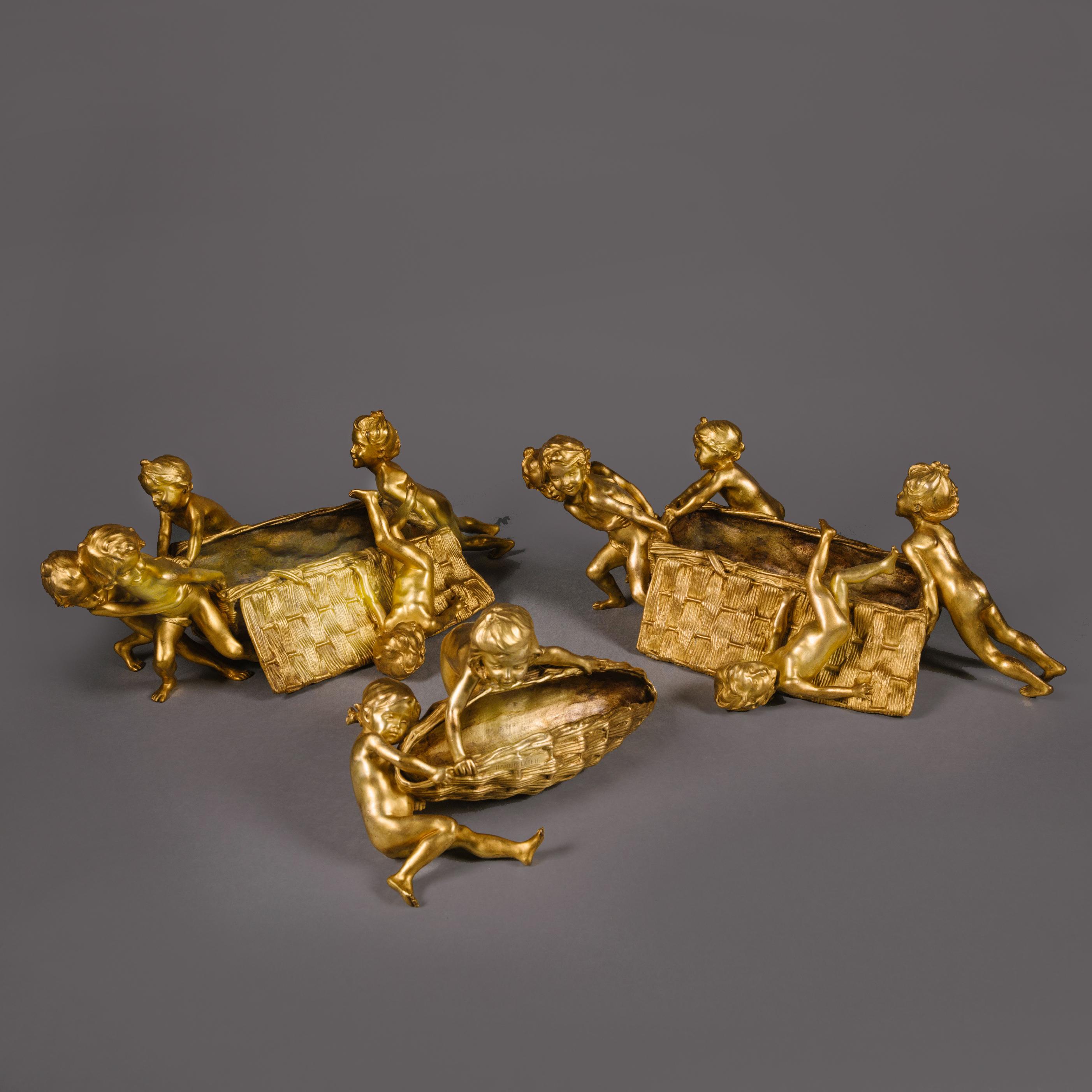 François-Raoul Larche (French, 1860 - 1912). 
Three 'Art Nouveau' Gilt-Bronze Sculptural Centrepieces. 

Comprising a large pair of centrepieces and a smaller single centrepiece. 

Each sculptural centrepiece modelled with children pulling