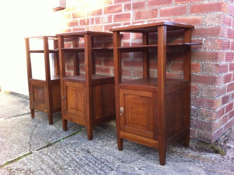 A near set of three French Arts & Crafts oak bedside cabinets with well designed extending shelves to each side perfect to store a bedtime book. With marble tops above and lower cupboards, one cabinet with a drop handle and the others with little