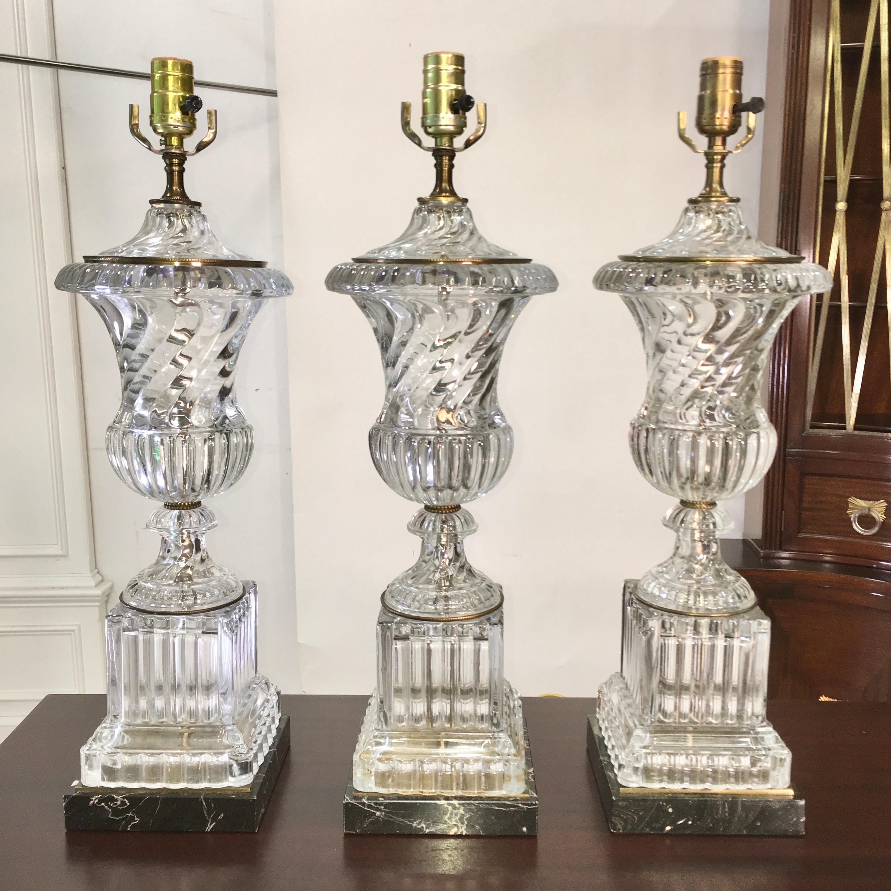 We have a total of three of these Baccarat style urn or vase form crystal lamps on square black veined marble bases with subtle bronze embellishments, by Paul Hanson Lighting Co. 
20 inches high from table to top of glass urn below socket. Diameter