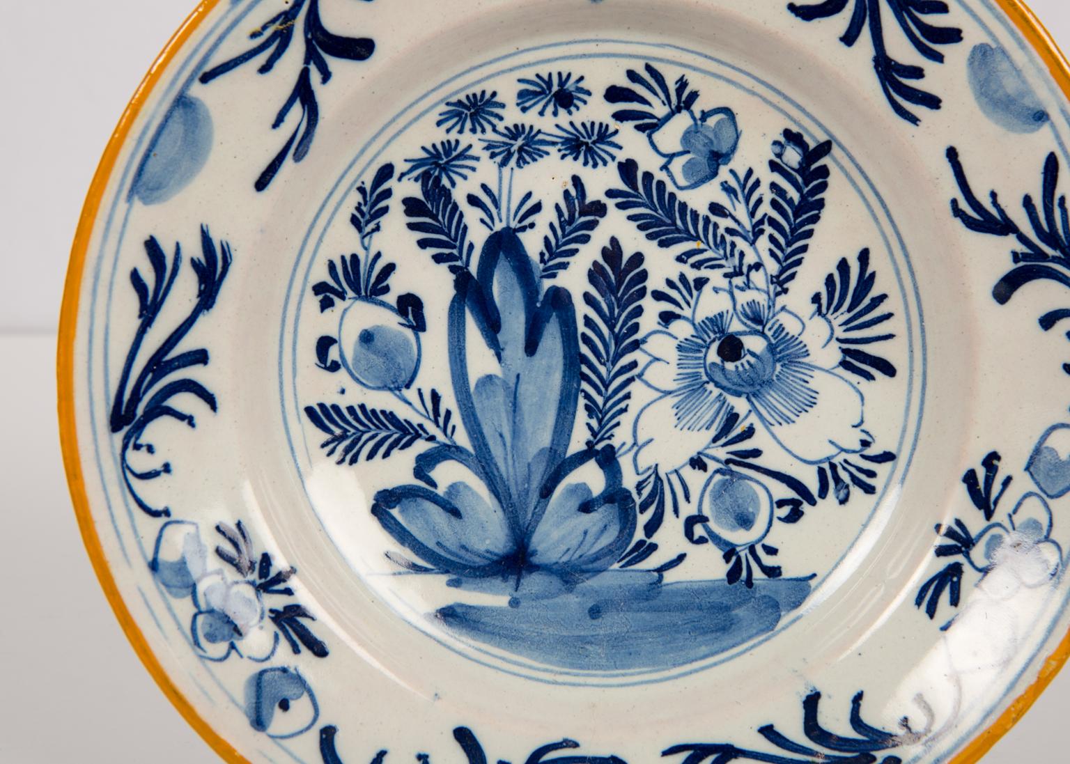We are pleased to offer this group of three brightly painted blue and white Delft dishes with mustard yellow slip painted edges.
Each dish shows a flower-filled garden scene. We see a large peony and other flowers.
The border is decorated with