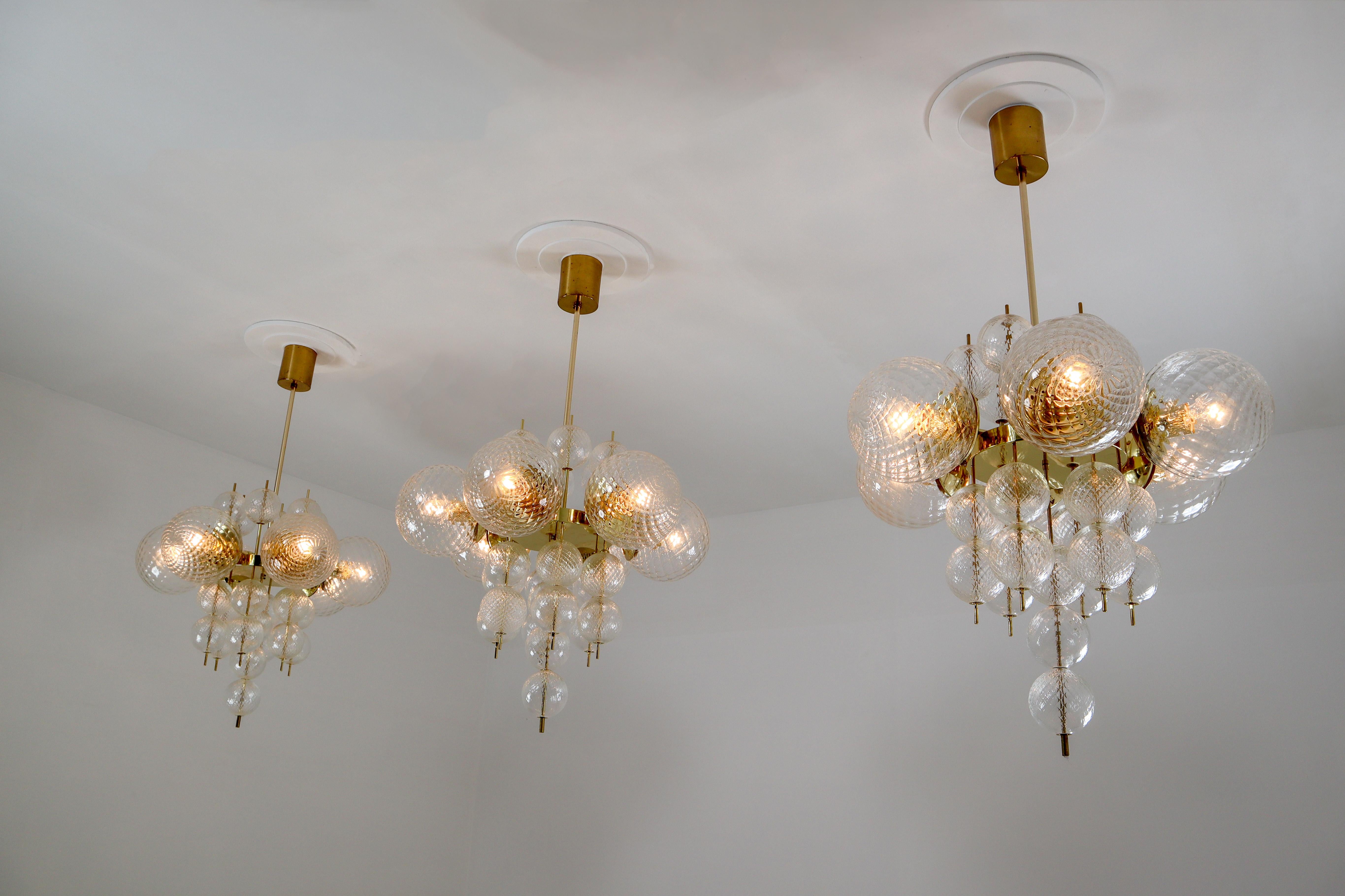 This set of three brass chandeliers was produced by Fa. Preciosa in Kamenicky Senov, Czechoslovakia in the 1970s. A spirited and chic design set of three chandeliers with brass fixture and art-glass. The chandelier with brass frame consist of six
