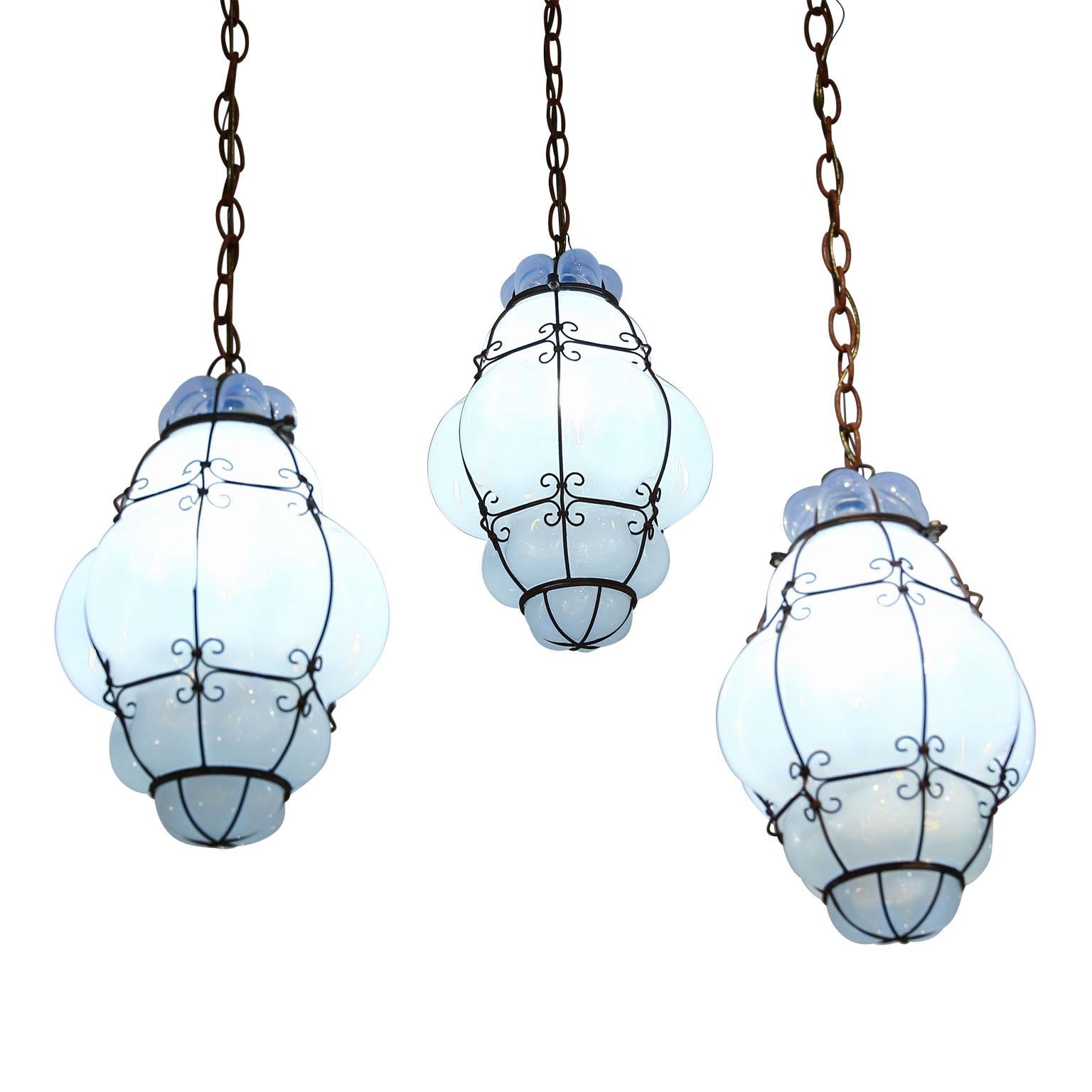 Three caged white glass Italian pendants, (circa 1930-1950). White glass turns a cool opal-like color when pendant is lit. Newly wired for use within the USA using all UL approved parts. Each pendant includes chain and a canopy (listed height does