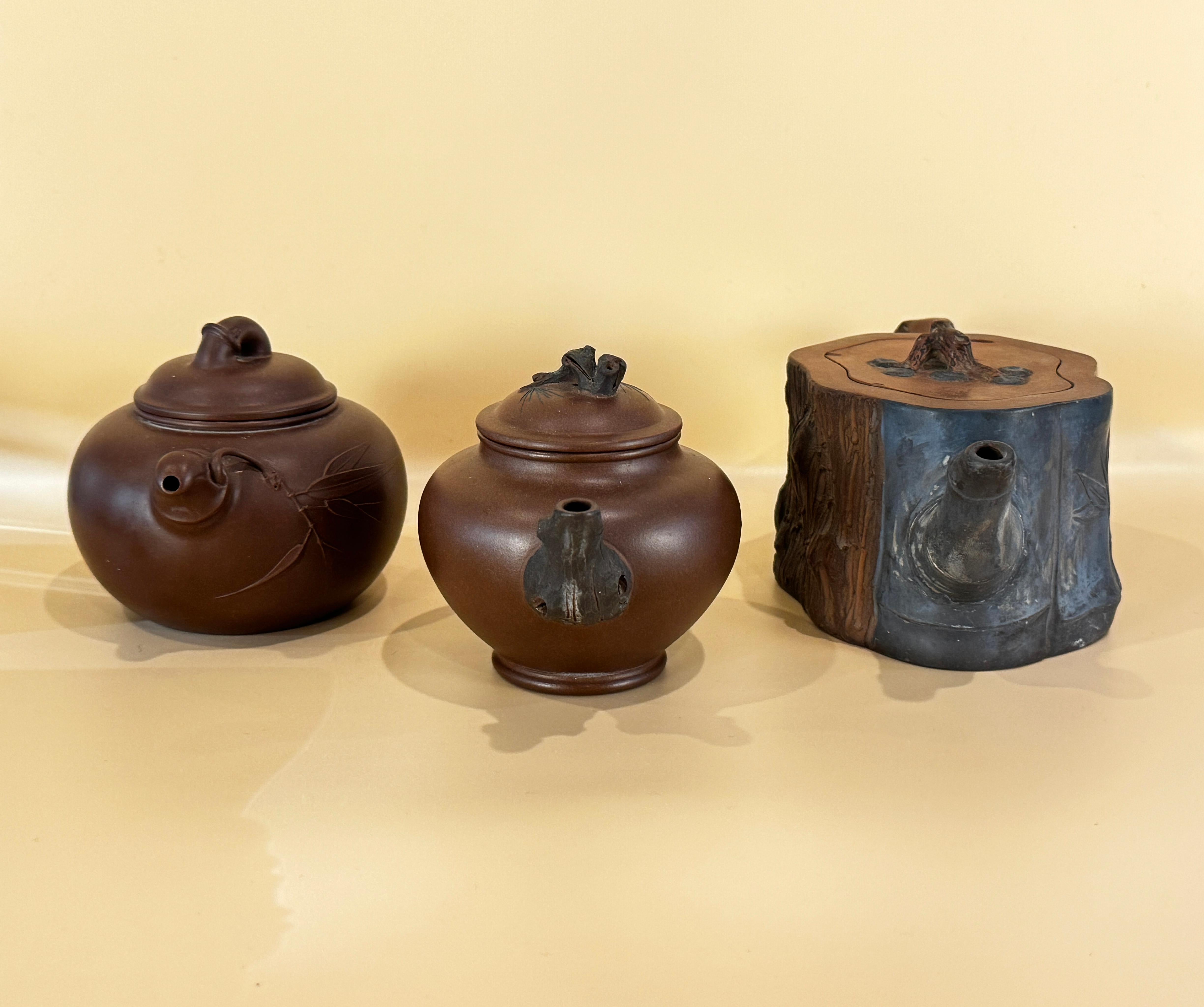 Three Chinese Yixing Clay Teapots, probably 20th Century. These charming teapots are beautifully formed of clay and varying in rich shades of brown and deep blue. Each is decorated with a bamboo theme. The largest pot decorated to show cherry