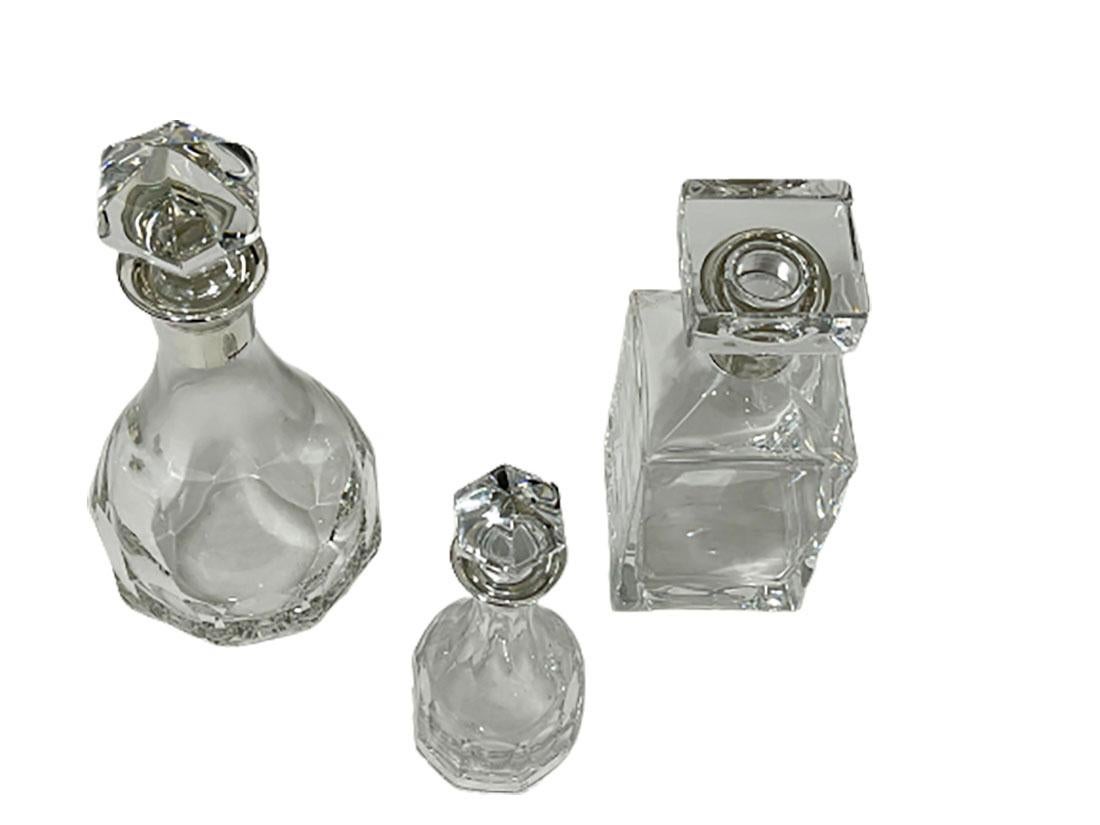 Three crystal with silver mounts decanters by Hermann Bauer, Germany. 

Three different decanters, in the shape of round, square and a small round size. The necks of the decanters with silver mounts have their silver hallmarks of Hermann Bauer,