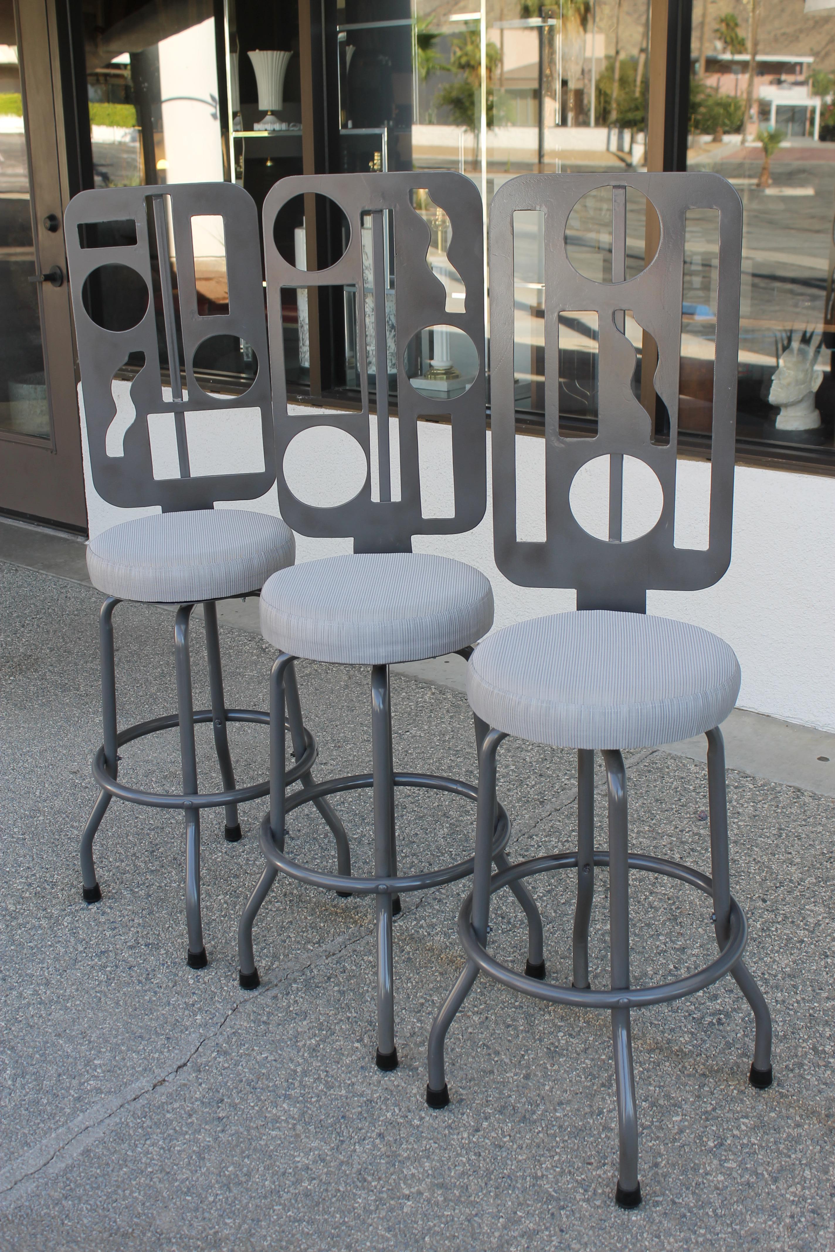 Three modernist studio made steel swivel bar stools. Each bar stool have different abstract patterns. We added new swivel mechanisms, had them powder coated and new sunbrella fabric seats. Seat cushions are 15” diameter. Seat height is 29