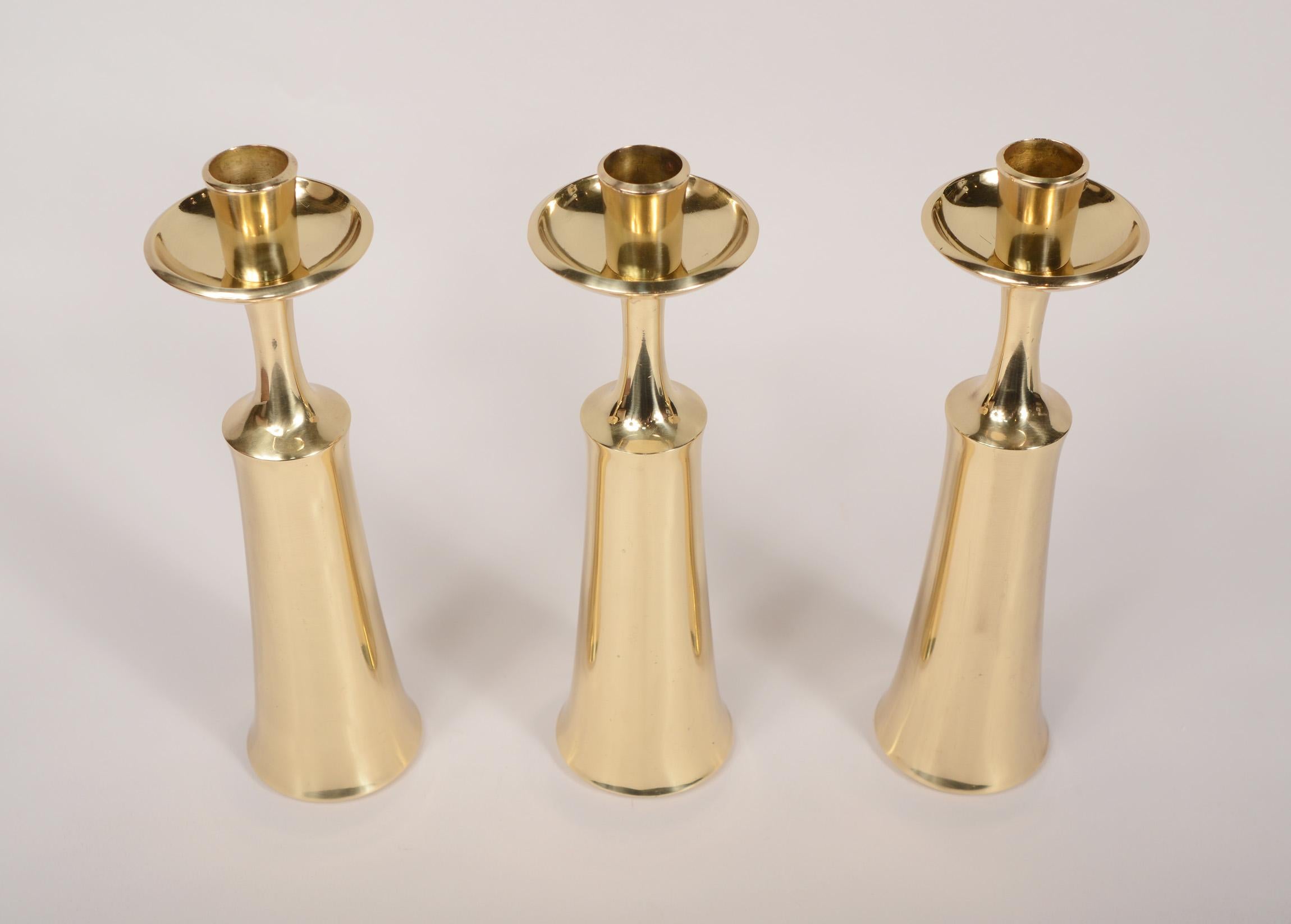 Set of three brass candle holders designed by Jens Quistgaard for Dansk. These have a very elegant modern design. The top portion of the candle holder can be removed and then with the piece turned over it becomes a bud vase.