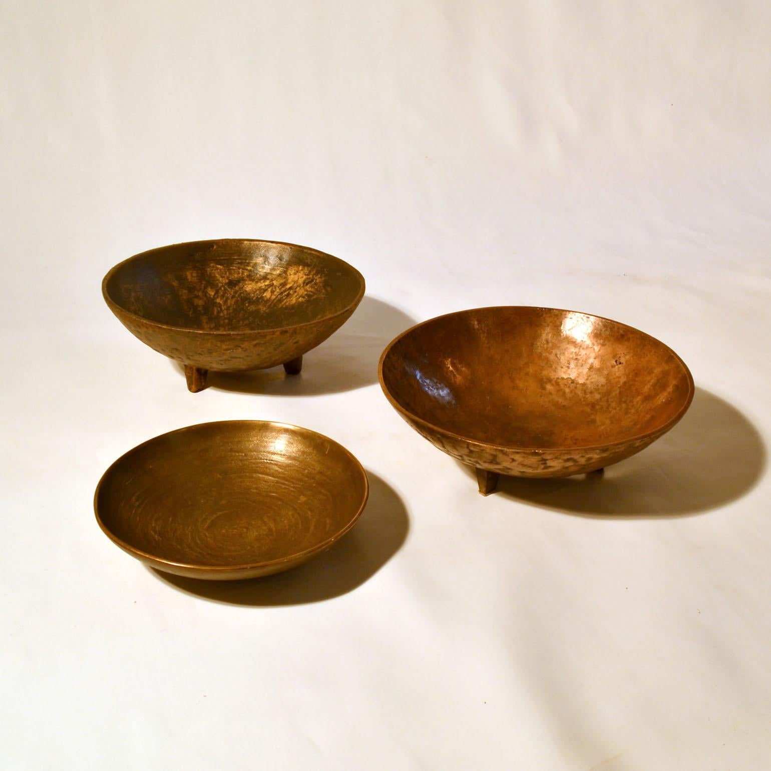 Set of three bronze cast bowls with subtle texture. Two are identical in shape on three legs with slightly different patina, and the third a bit smaller signed Pabst 173.