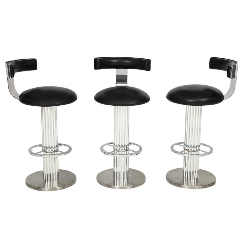Designs for Leisure Bar Stools, Chrome and Leather Swivel. Three heavy swivel barstools with high polished steel backrests and foot rests, polished aluminum reeded columns and brushed steel bases. Upholstered in black leather. In good original