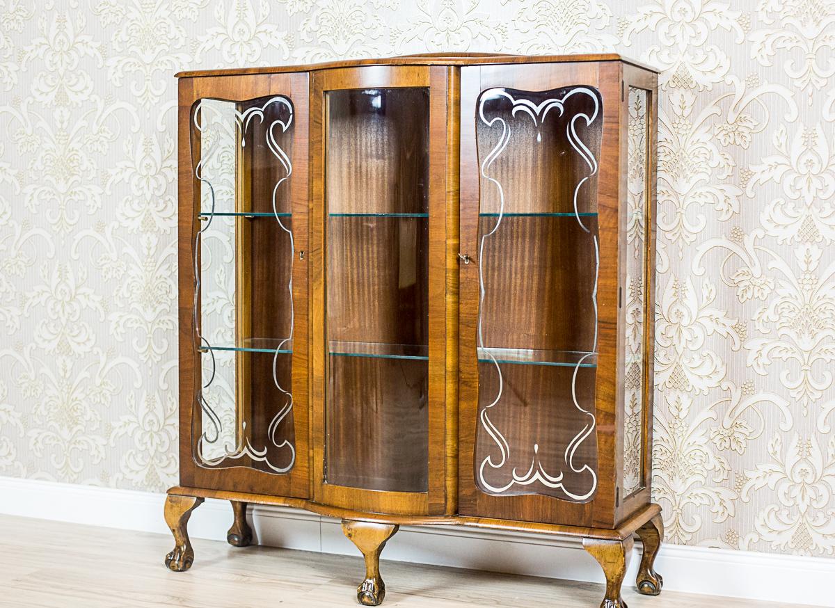 Display Cabinet in the Chippendale Style Circa 1960

A modest-sized, three-door display cabinet from the 2nd half of the 20th century. The piece is supported by curved legs ending in bird claw-shaped balls. The sides and front doors are glazed, with