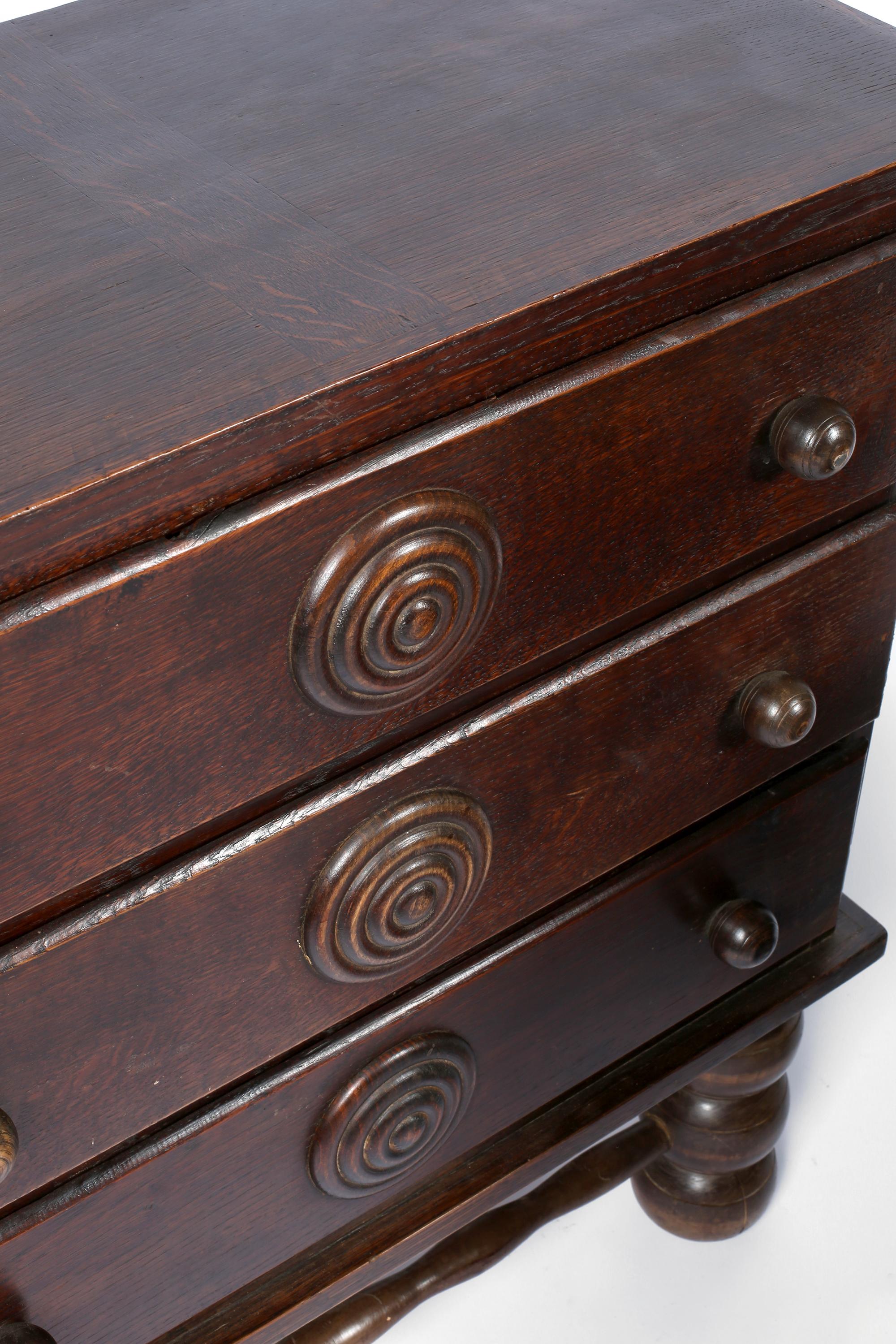 A three drawer chest of drawers by modernist designer Charles Dudouyt (1885-1946). Constructed from dark stained solid oak, featuring substantial bobbin turned legs and bulls eye detailing to the drawers. French, circa  1940.