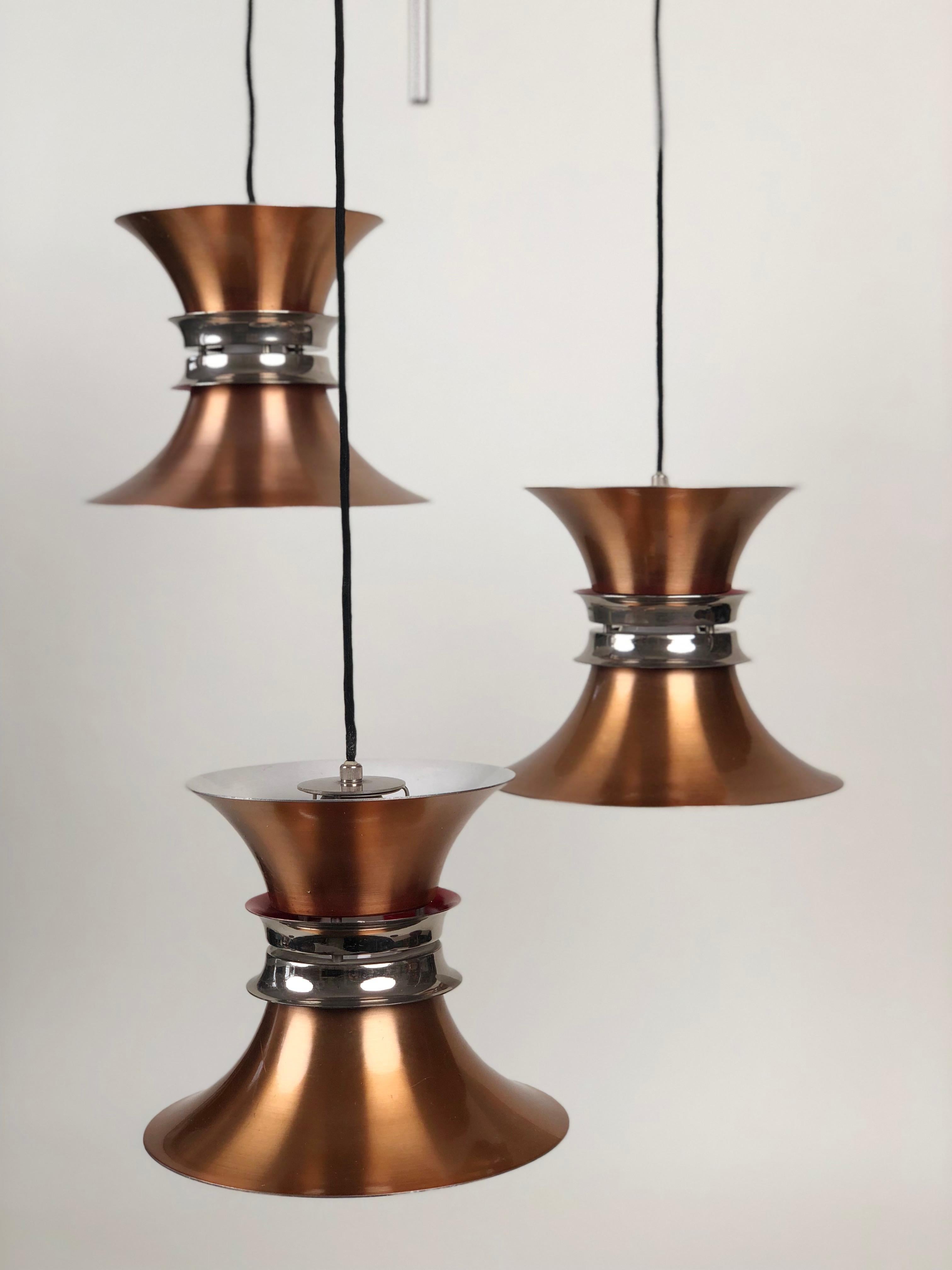 A rare three element pendant lamp designed by Carl Thore for Granhaga Metallindustri. This example is part of the Trava series.
It consists of three lamps, each composed of stacked elements in anodized copper, with white reflected surface, then two