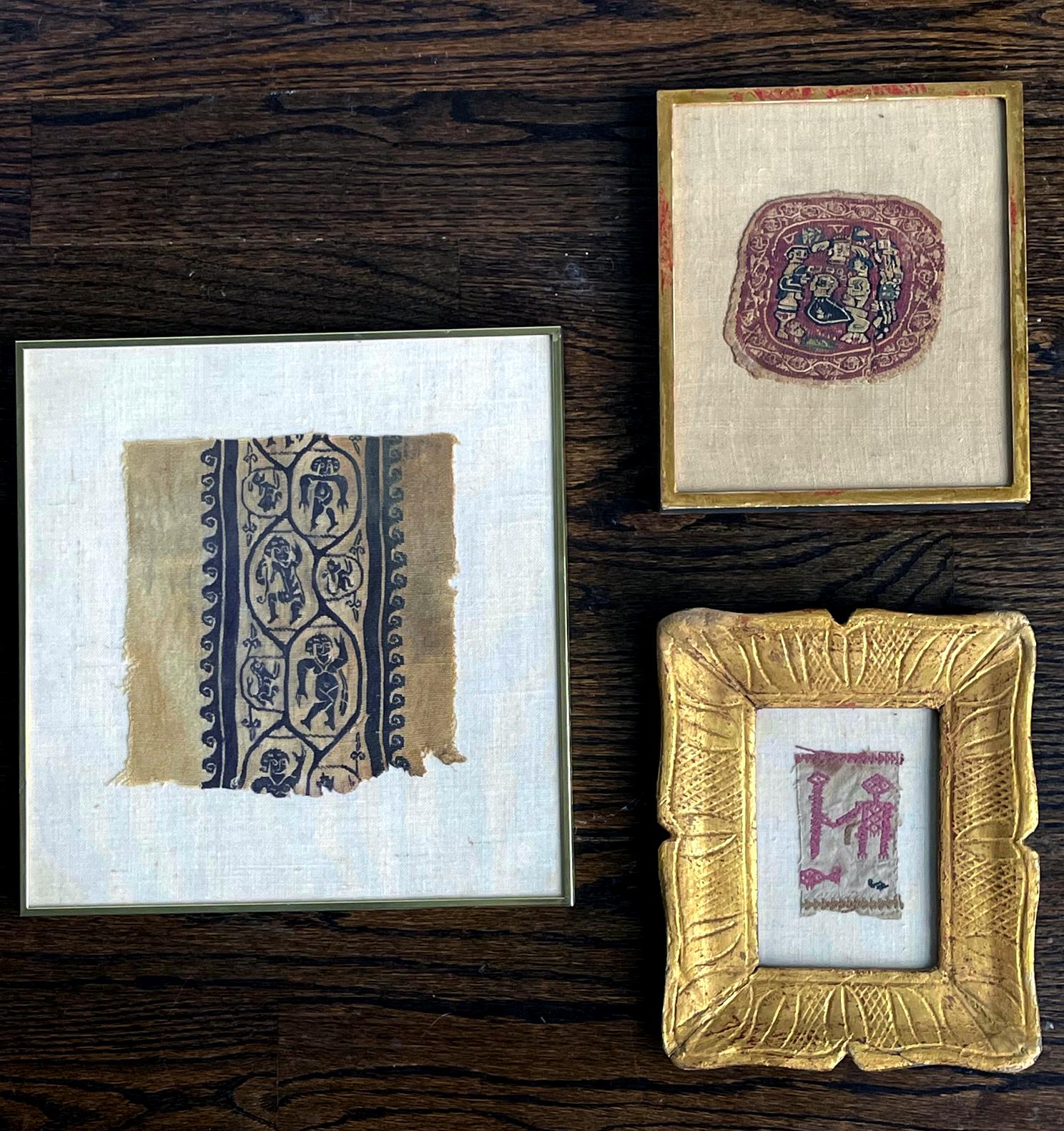 A collection of three antique textile fragments displayed in various frames. It consists of a blue on white woven panel presented in a metal frame. The panel depicts dancing human figures and lions in repeating pattern and bordered by scrolling