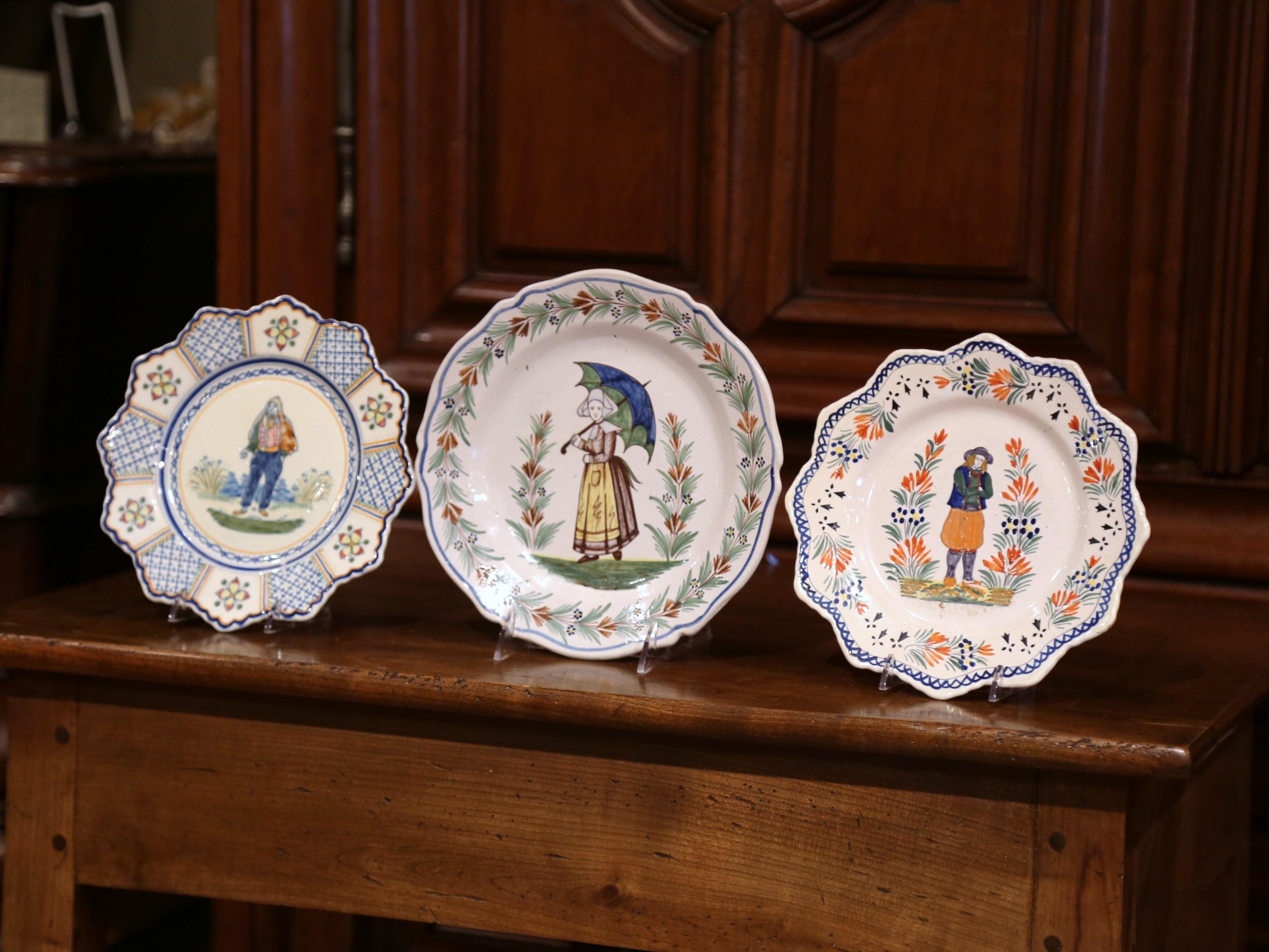 Decorate a cabinet or a shelf with this set of three ceramic plates from Brittany. Crafted in Quimper, circa 1930, each colorful plate is beautifully hand painted and features traditional Breton figures along with floral decor embellishment. The