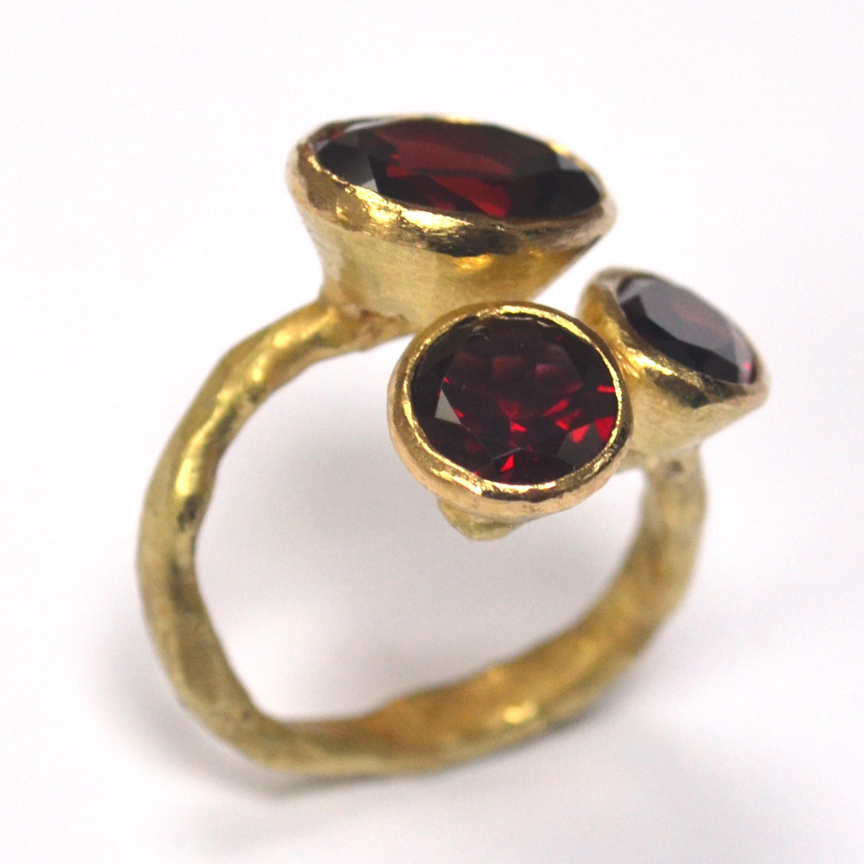 18k yellow gold handmade organic texture open ring with three garnet cluster.

The garnets in this ring are a beautiful true red, cut so that flashes of red glint away in any light. The band has been made using Disa Allsopps signature reticulation