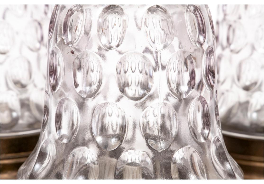 Satz von drei Glocken aus klarem Pressglas mit eingekerbtem, abgestuftem Daumenabdruck, vermessingtem Kragen und Endstück mit Kugel aus Messing. Die Halterungen sind elektrisch und nehmen eine Glühbirne mit drei Schrauben auf, die sich zum