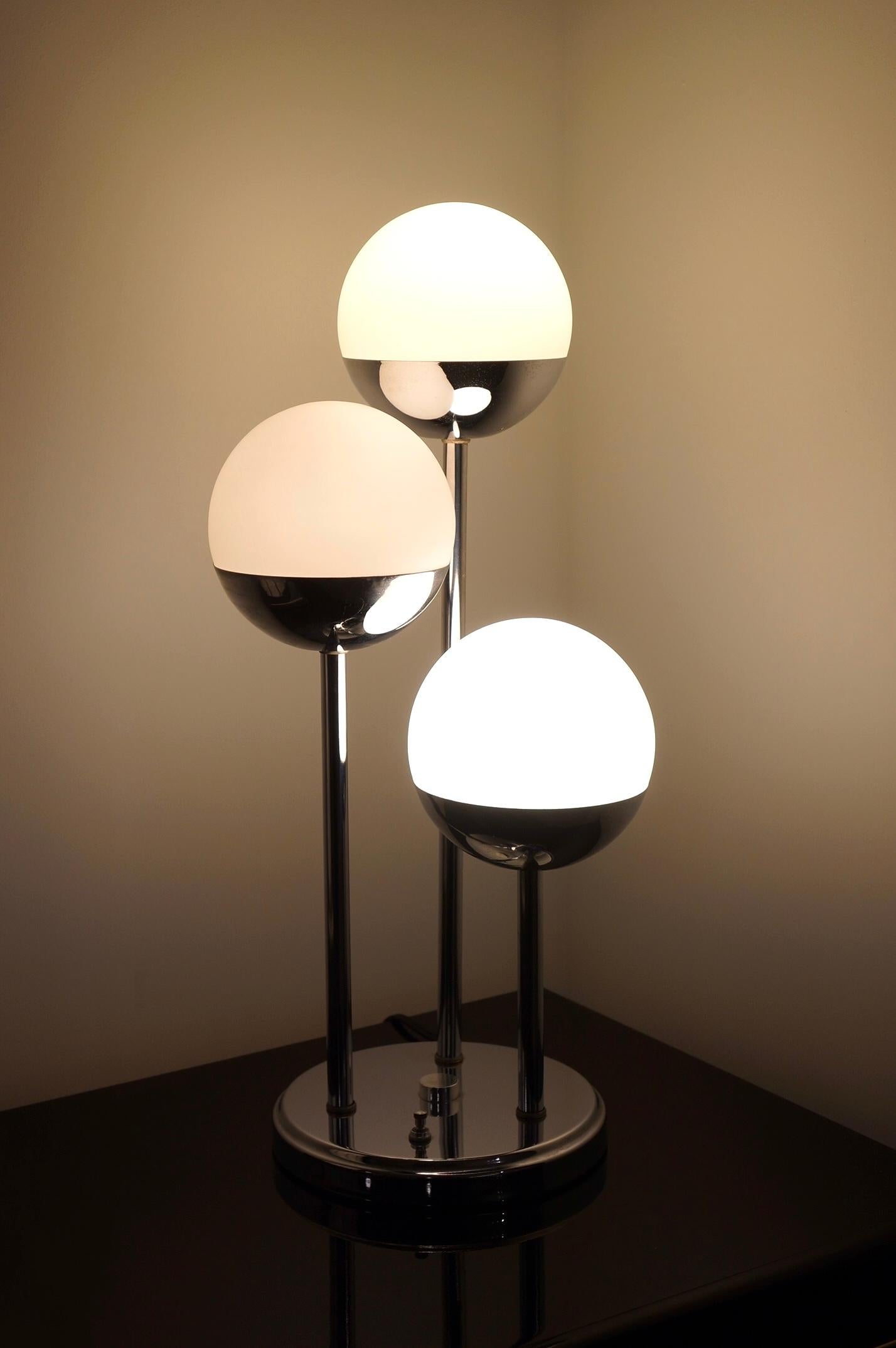 Space age style chrome table lamp with three globes. It was made in the 1970s. The base is chrome and the three globes are finished in milk glass. It’s three tiered in varying heights. It has three switches with an option to light one globe, two
