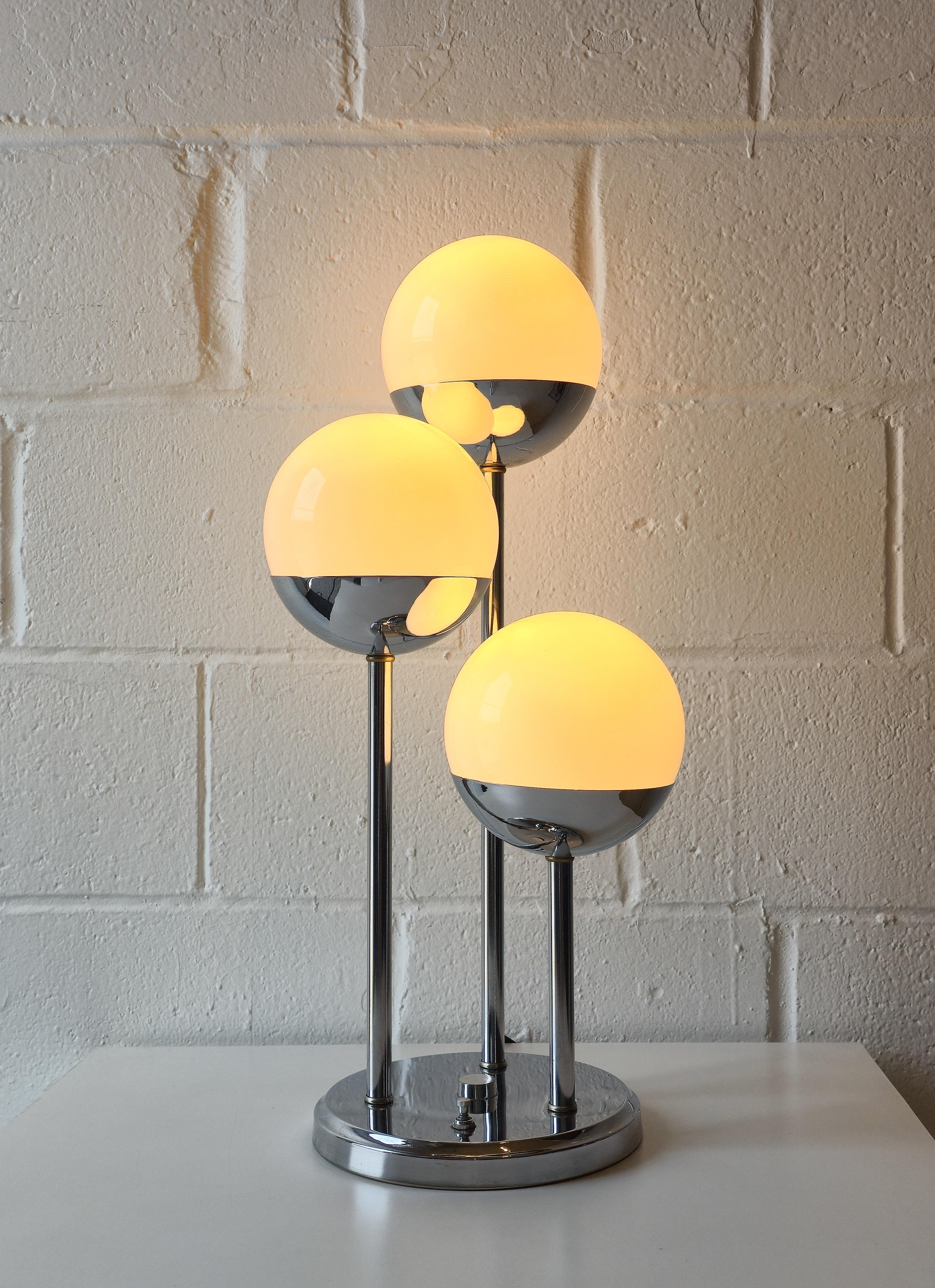 Verchromte Tischlampe im Space-Age-Stil mit drei Kugeln. Sie wurde in den 1970er Jahren hergestellt. Der Sockel ist verchromt und die drei Kugeln sind aus Milchglas. Sie ist dreistufig und unterschiedlich hoch. Sie verfügt über drei Schalter, mit