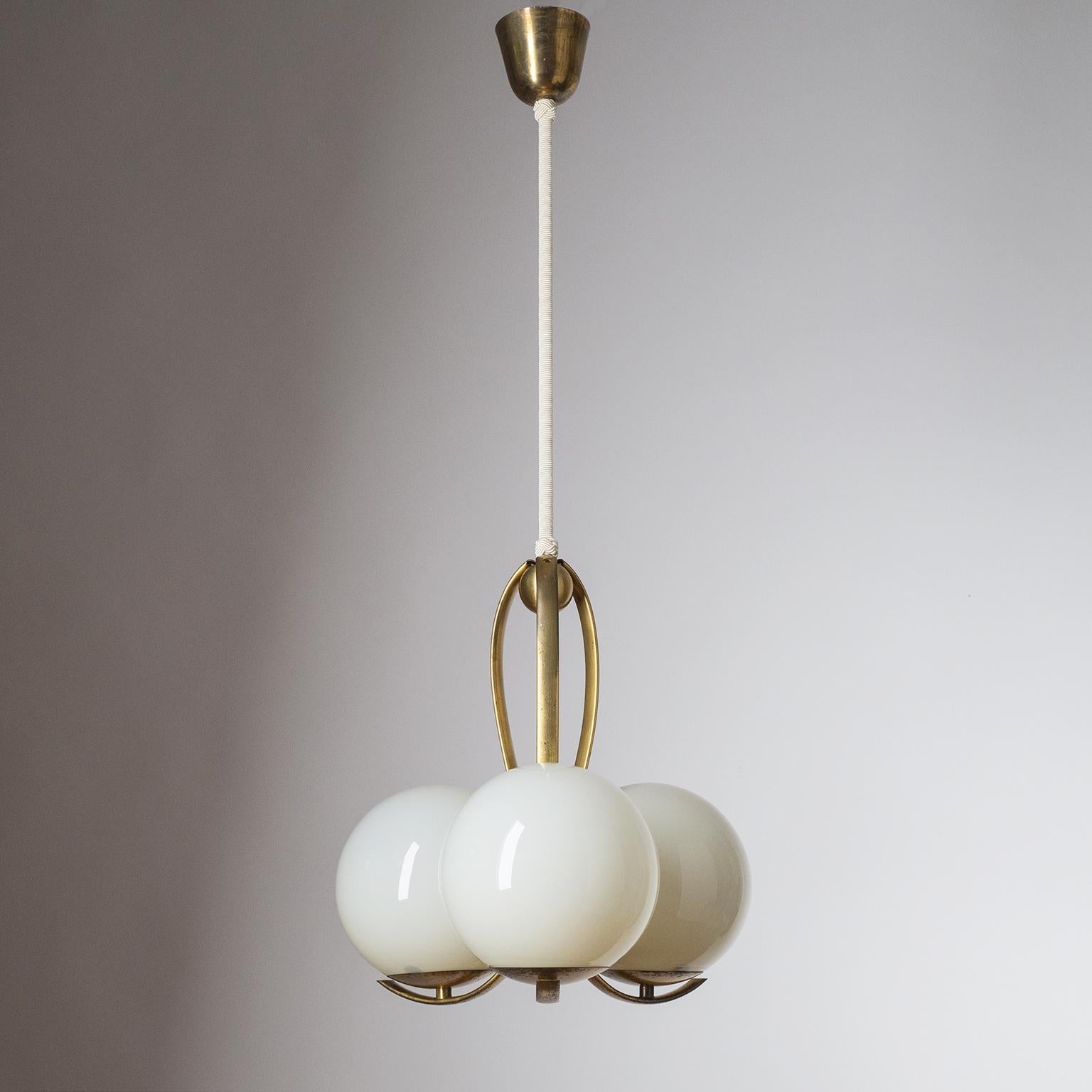 Rare three-globe Art Deco chandelier, circa 1930. Blown ivory-colored glass diffusers on curved brass hardware. Original bakelite E27 sockets with new wiring.