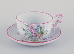 Three hand-painted tea cups and saucers in faience with motifs of flowers.