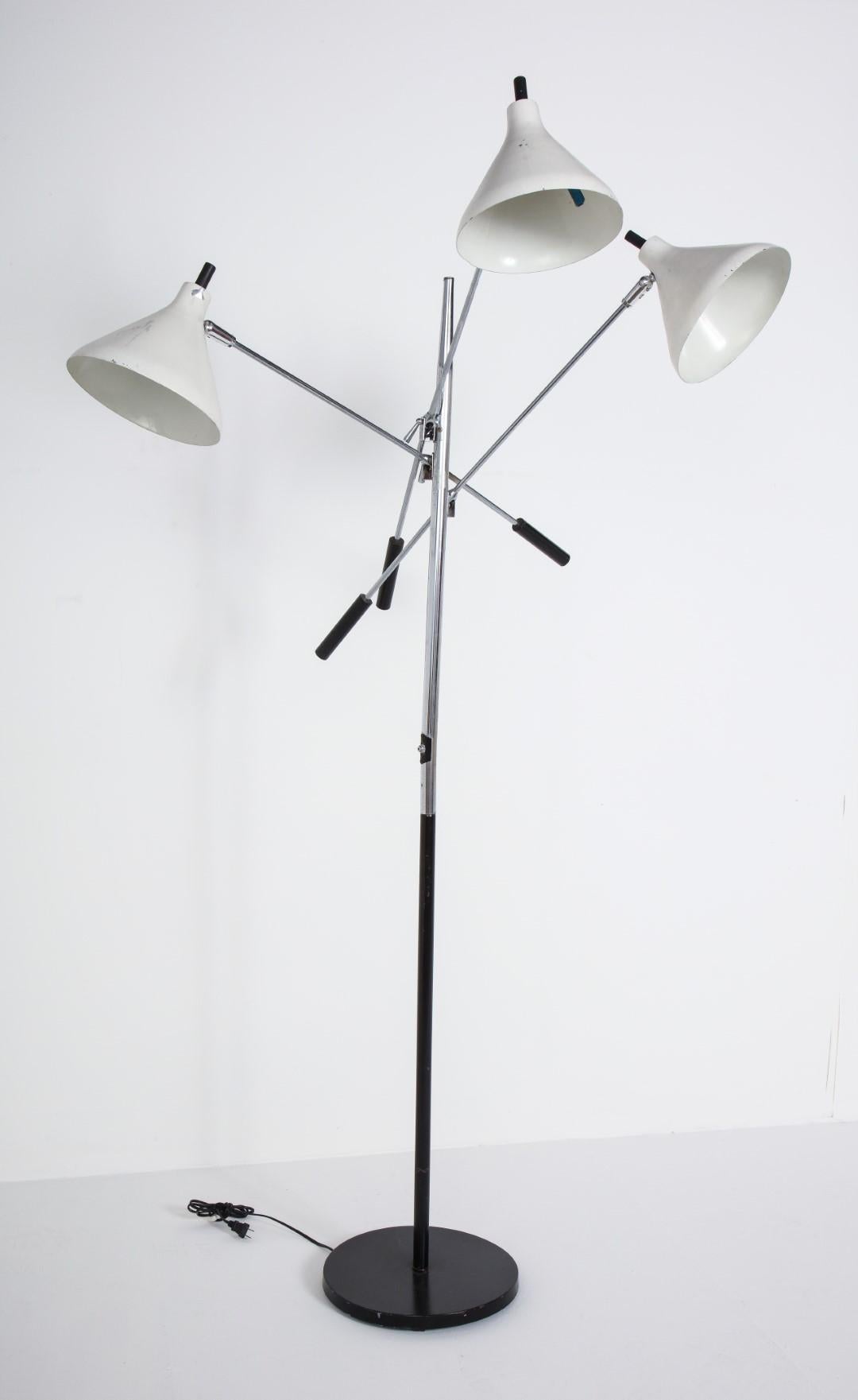 Floor lamp with three heads with white shades and chrome posts. Adjustable, with a black circular base. Each head has its own on/off switch for adaptable lighting. Sticker on base: Underwriters Laboratories Portable Lamp, Issue No. 77575,