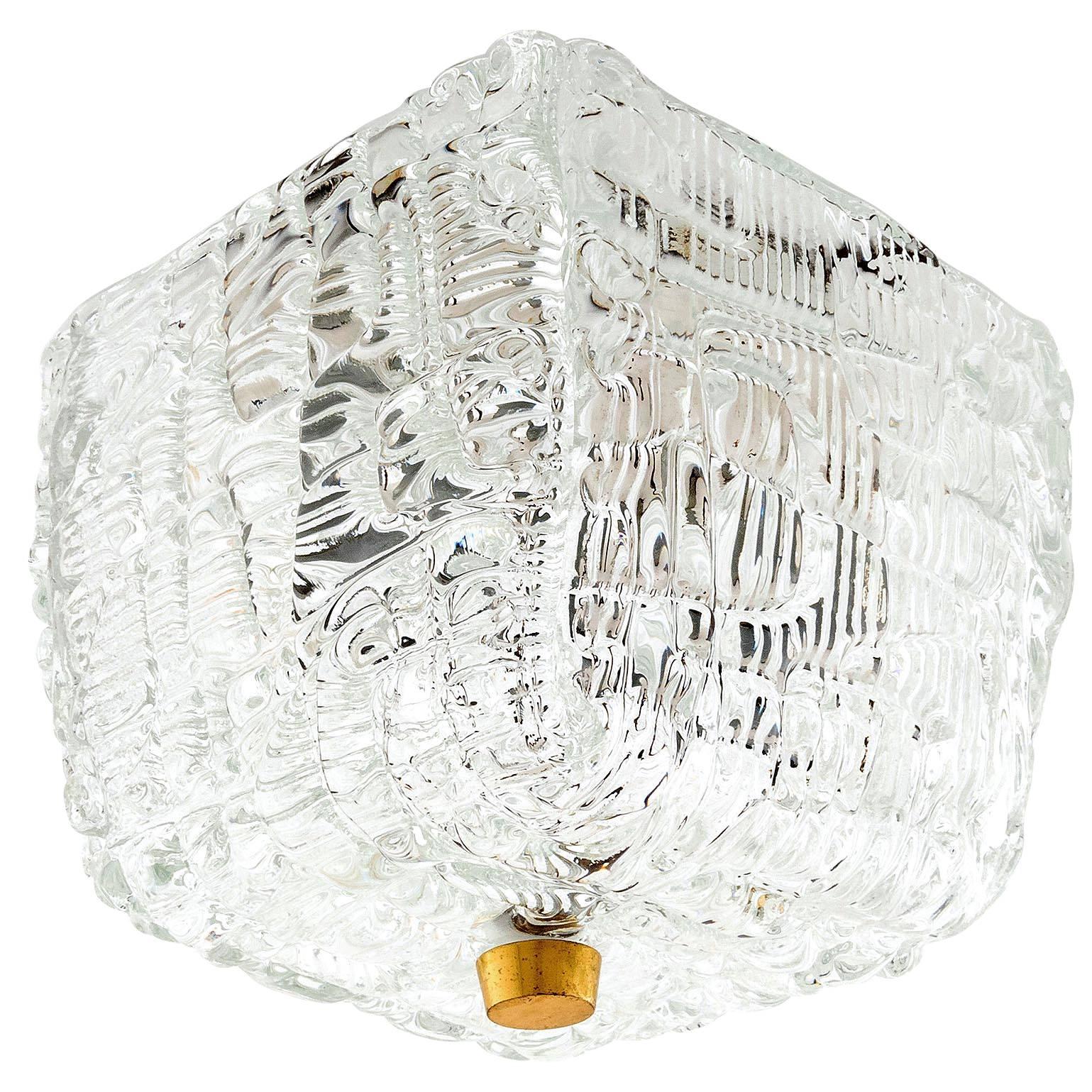 One of three square flush mount light fixtures by Kalmar, Austria, manufactured in Mid-Century, circa 1960 (late 1950s or early 1960s). 
A textured clear glass is mounted with a brass knob to a backplate. 
The lamp has two sockets for small screw