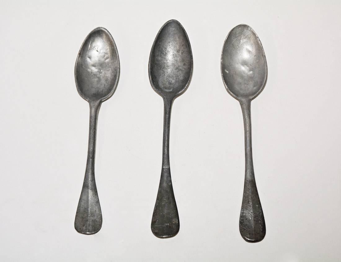 The three large pewter soup spoons are handcrafted and have flared and ridged handles with stamped oval shapes on the undersides.