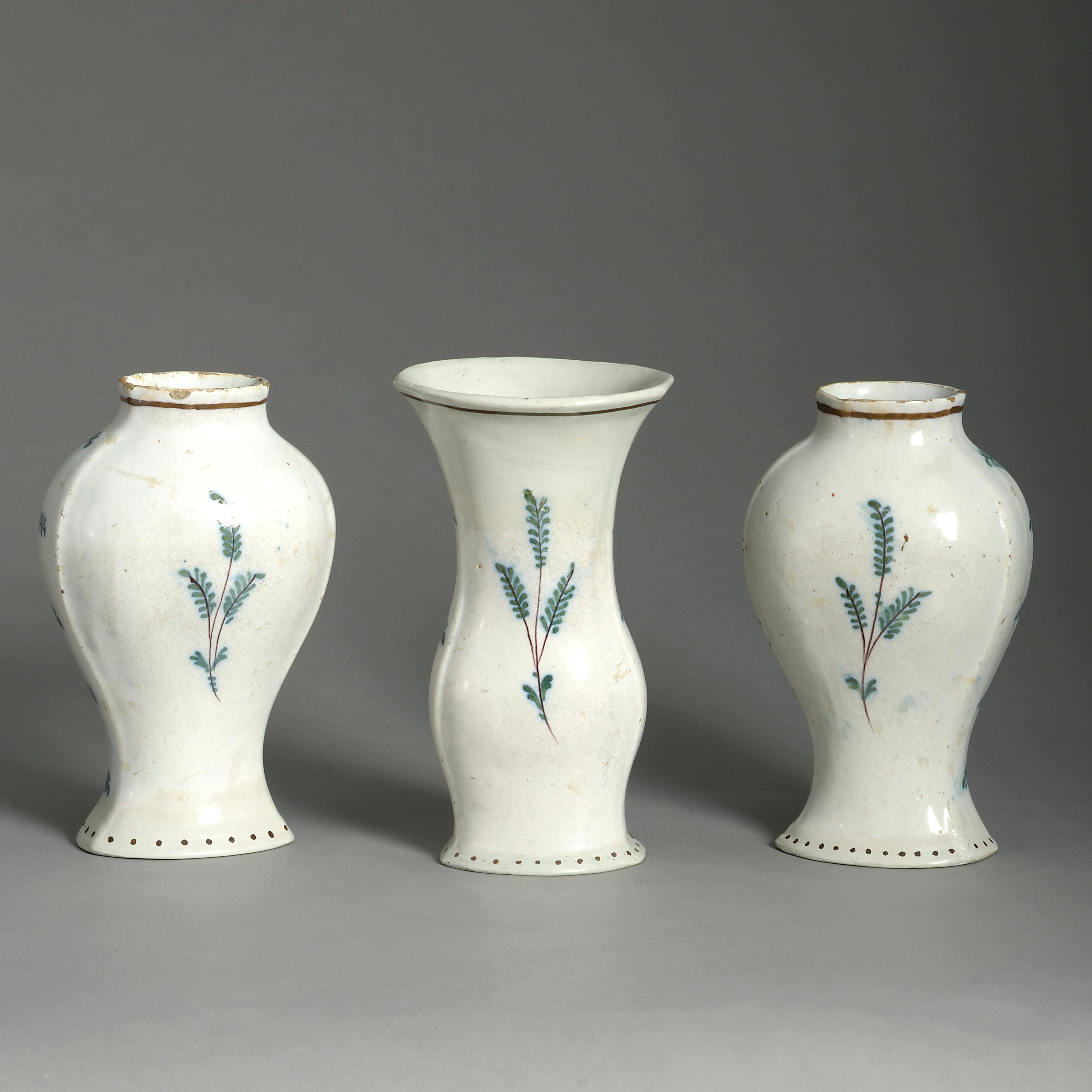 Three late 18th century polychrome glazed Delft pottery vases, two of baluster form, one of trumpet form, each with a central cartouche depicting a landscape upon a yellow fish scale ground.