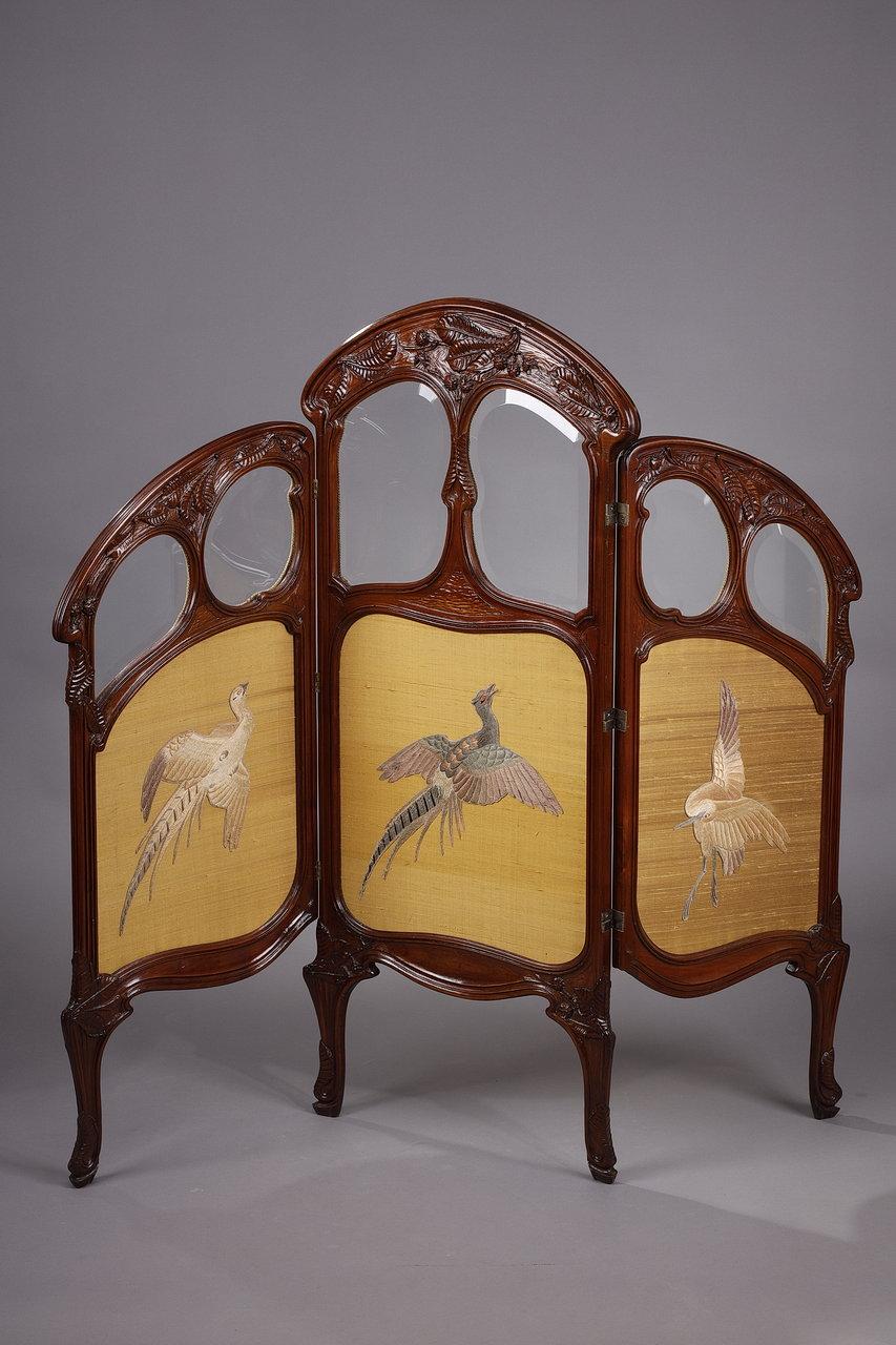 Charming Art Nouveau period small three-leaf screen or mantel screen in carved mahogany decorated with embroidery on silk representing birds. The wooden panels are carved with stylized leaves and chestnut fruits. Each leaf is decorated with a bird