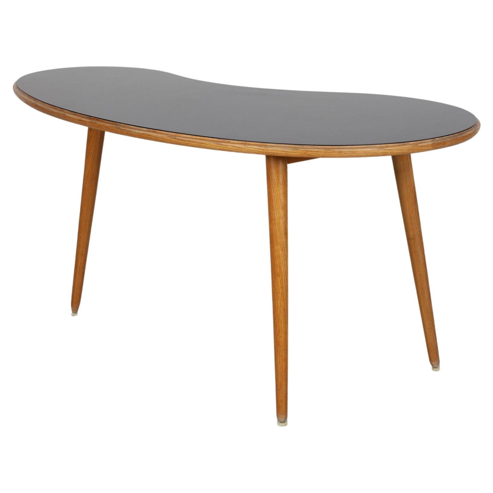 Three-legged, kidney-shaped coffee table with a black Formica surface 1950s For Sale