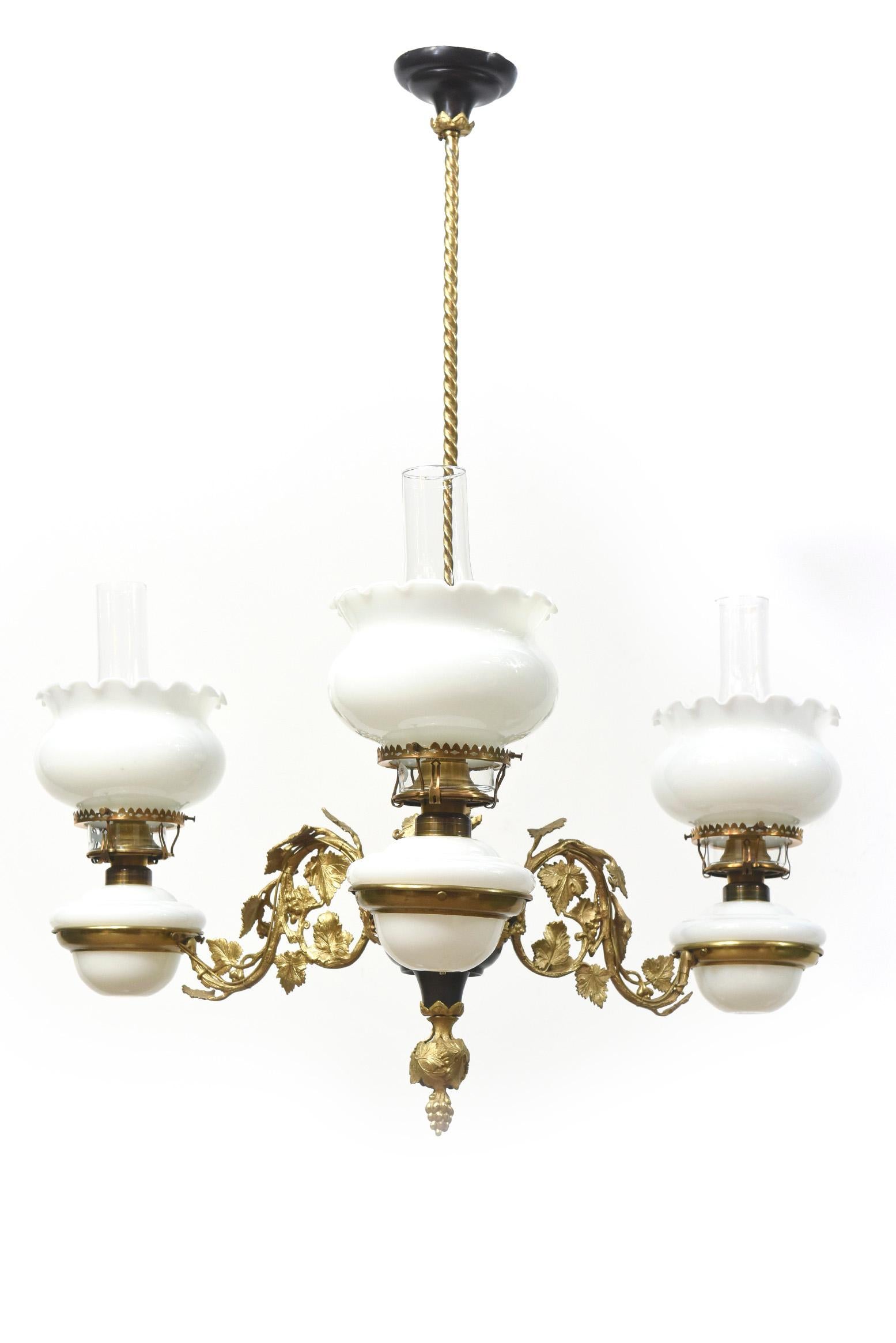 A lovely gilded era oil chandelier. Made by Henry Hooper C. 1870. Fine castings of grapevines on arms in gilt bronze. Brass body with a dark patina. White Glass shades and Oil Fonts. Suspended from a slender roped tube. Rococo Revival. American.