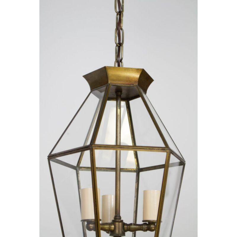 Three light lantern with antique brass finish. Clear glass panels with a thin brass frame. The crown is hexagonal brass and the bottom rim is decorated with a filigree band. C. 1950. Completely restored and rewired. Three lights, 60 Watt max each.