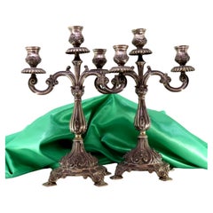 Three-light silver candelabra with shells and garlands resting on raised bases Three-light silver candelabra with shells and garlands resting on raised bases