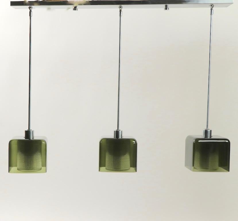 Chic architectural light fixture attributed to Carl Fagerlund for Orrefors. This chandelier has a minimalist brushed steel frame with drop three arms that support smoked green/ gray green glass shades with clear textured glass cylindrical interior