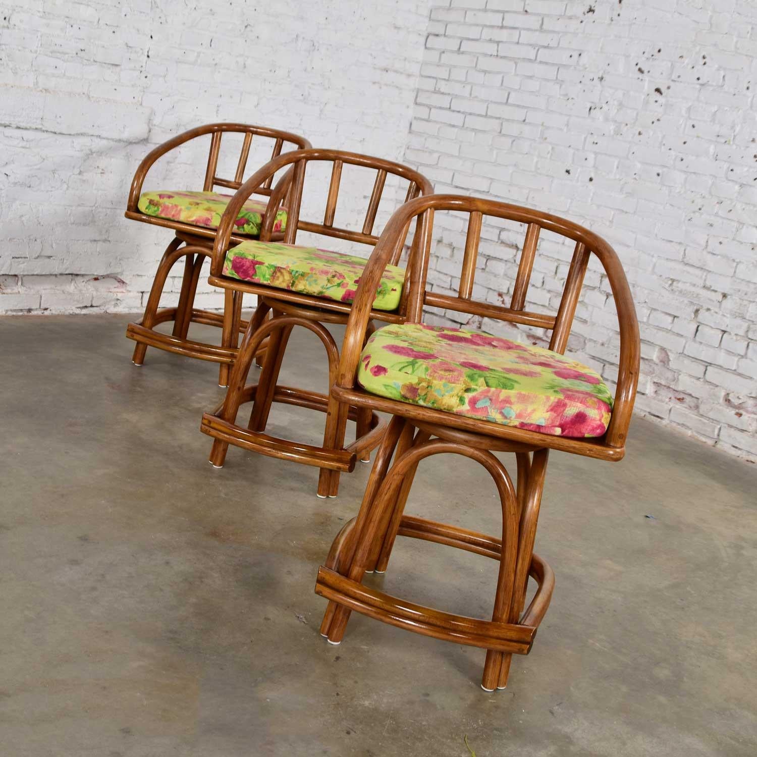 Wonderful set of three Mid-Century Modern rattan swivel counter height bar stools by Rattan Specialties Inc. Comprised of rattan and floral print removable seat cushions. Beautiful condition. We have touched up the arms where they were slid under a
