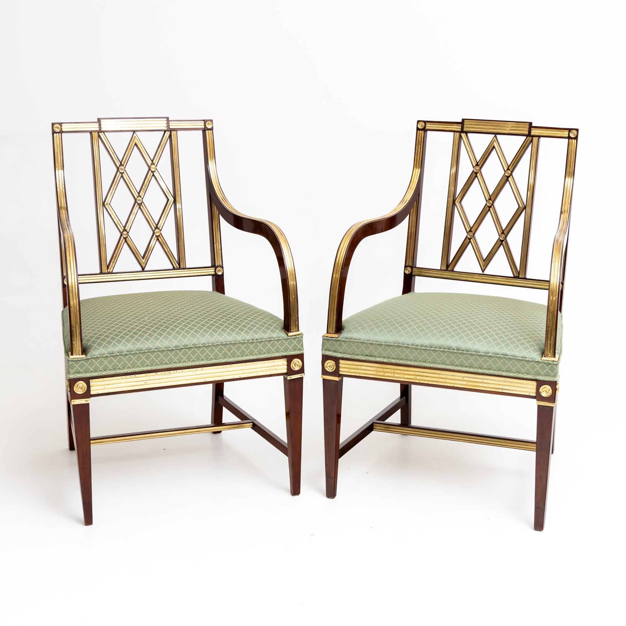 Set of three neoclassical armchairs made of mahogany with brass decoration and diamond-shaped strutting in the backrest. The chairs stand on square tapered legs with H-shaped struts. The seats are upholstered in a fine light green fabric with a gold
