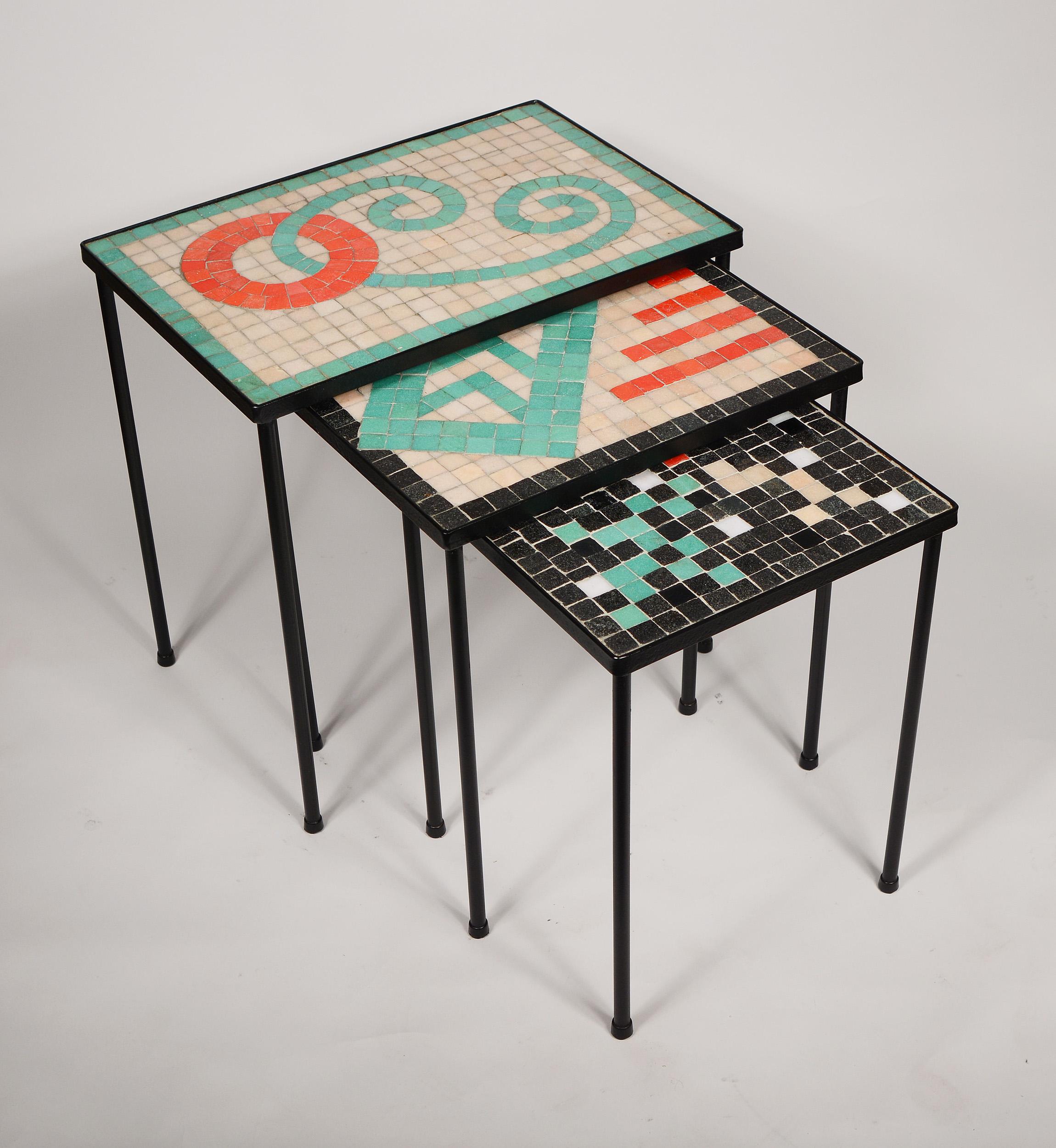Three small nesting iron tables with mosaic glass tops. The abstract designs on the tops are outstanding. The iron has been repainted. The grout has staining. There are small chips to a few tiles. The large table is 18.25 inches wide, 12.25 inches
