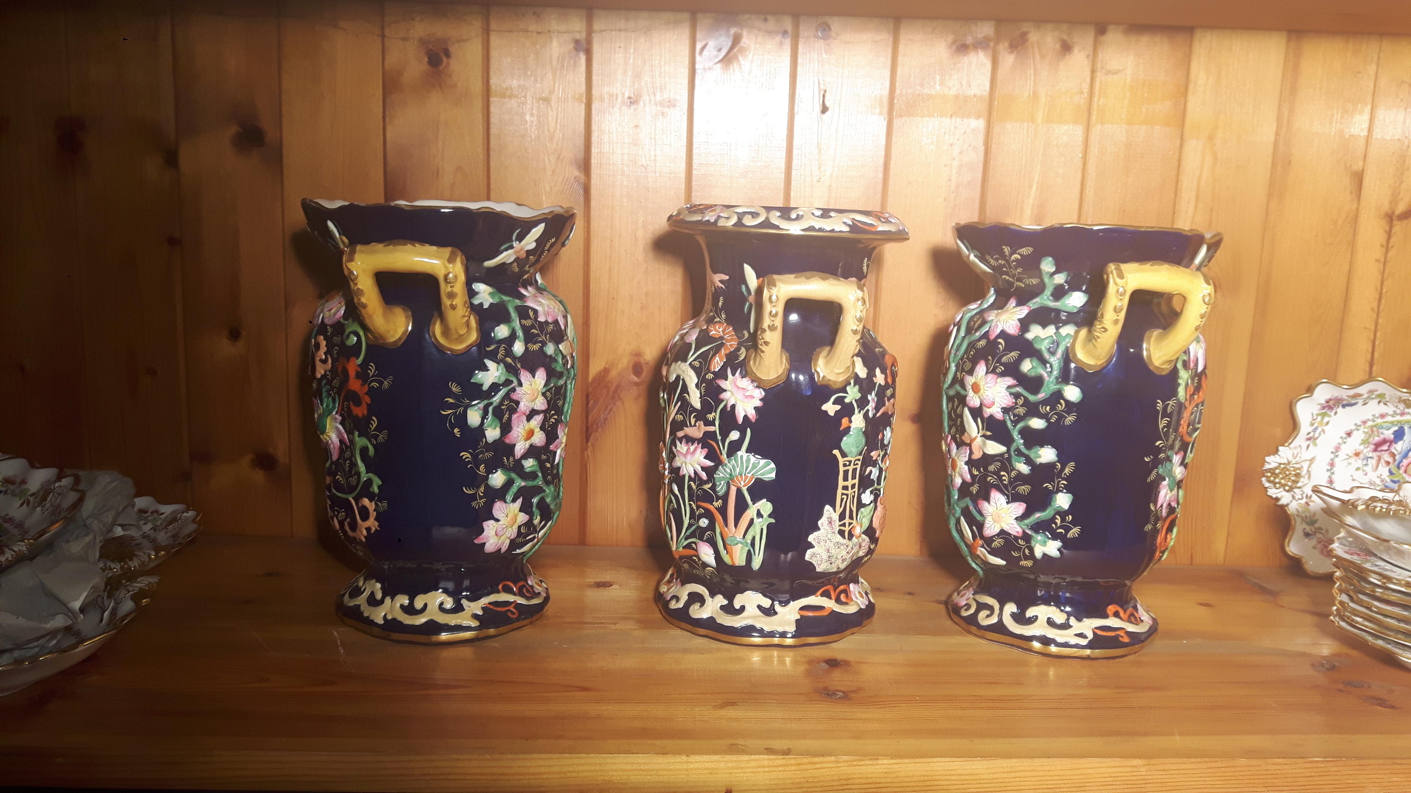A trio of Oriental style English vases, on a blue background, hand painted with embossed chinoiseries style urns and flowers in the Mason style.