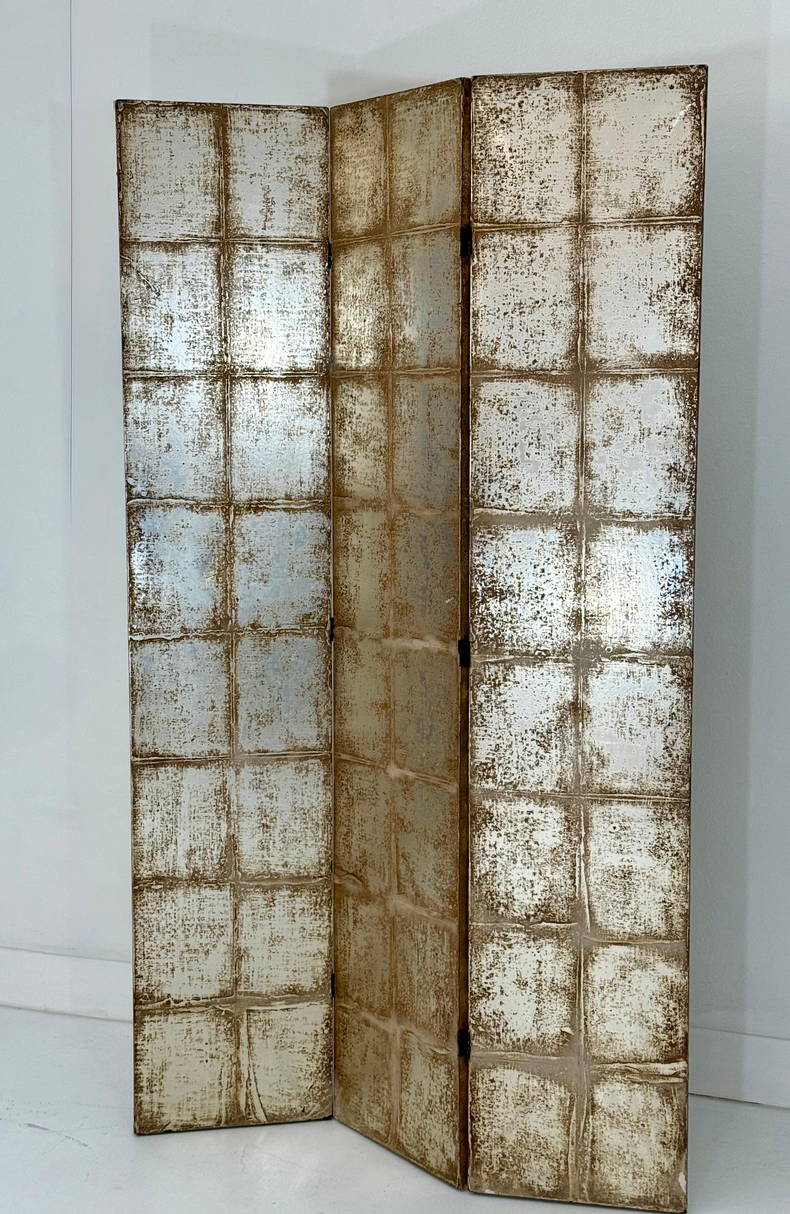 This sophisticated three-panel silver tea leaf folding screen is a striking decorative element, finished on both sides for maximum versatility. The front features a grid of rectangular panels, hand-applied with silver tea leaf and subtly distressed