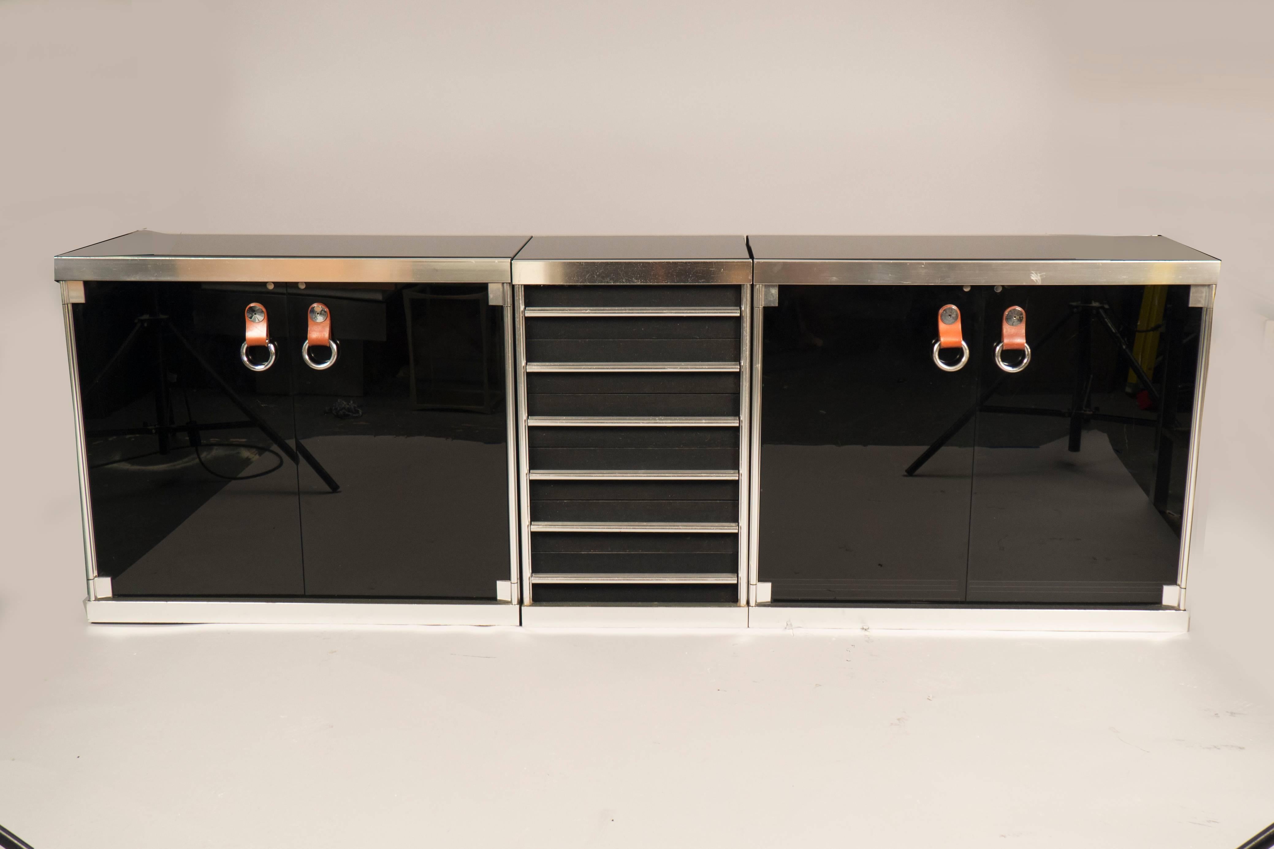 Steel and glass sideboard comprising two cabinets with smoked glass doors and leather pulls on each side, the middle features six drawers. New glass tops have been added.
 