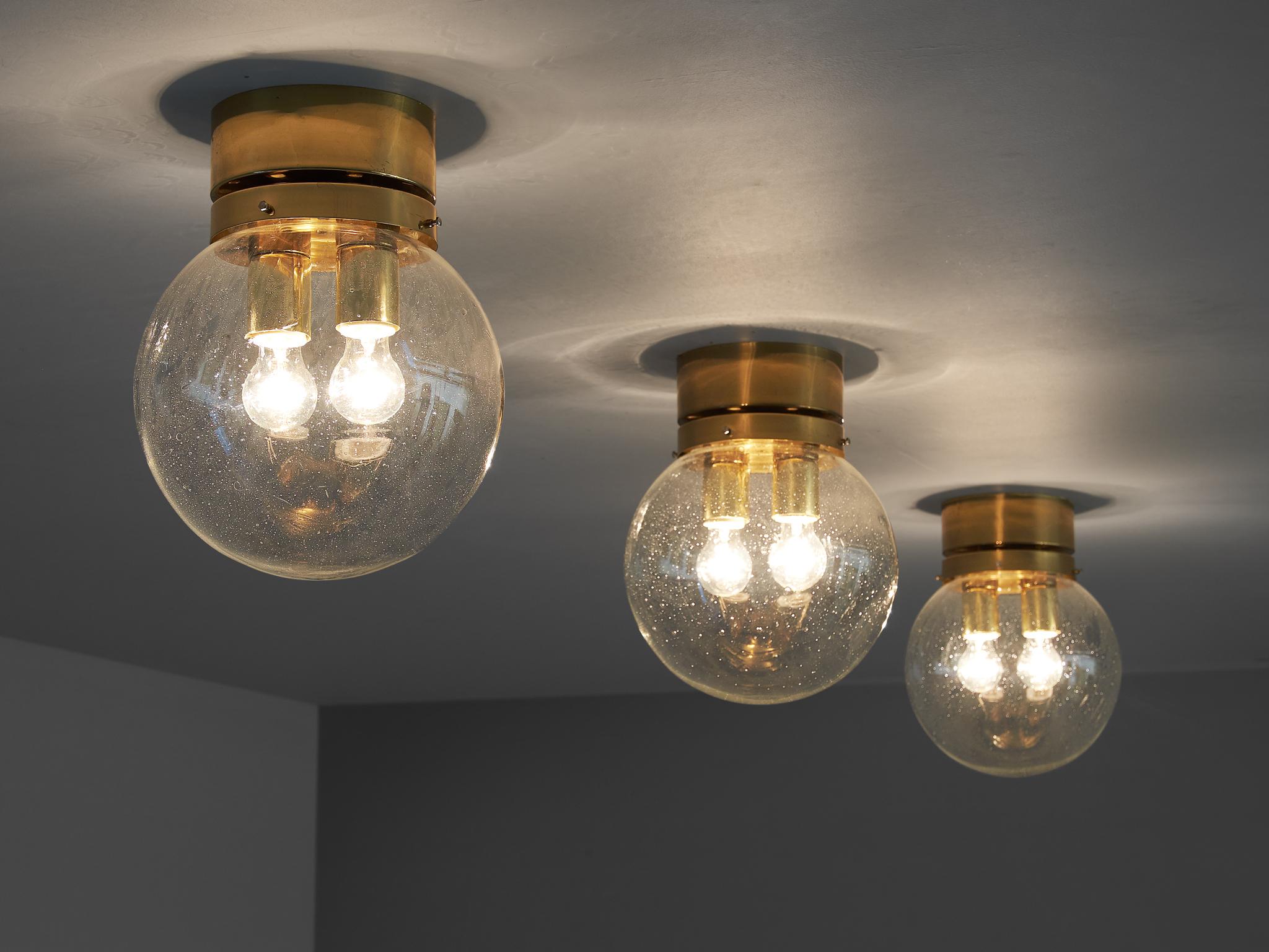 Three flush mount lights, in glass and brass, Europe, 1970s.

Set of modern and minimalistic ceiling lights in brass and glass. Each light consist of a round brass fixture and a raindrop glass sphere. Inside the sphere are two light-points. The