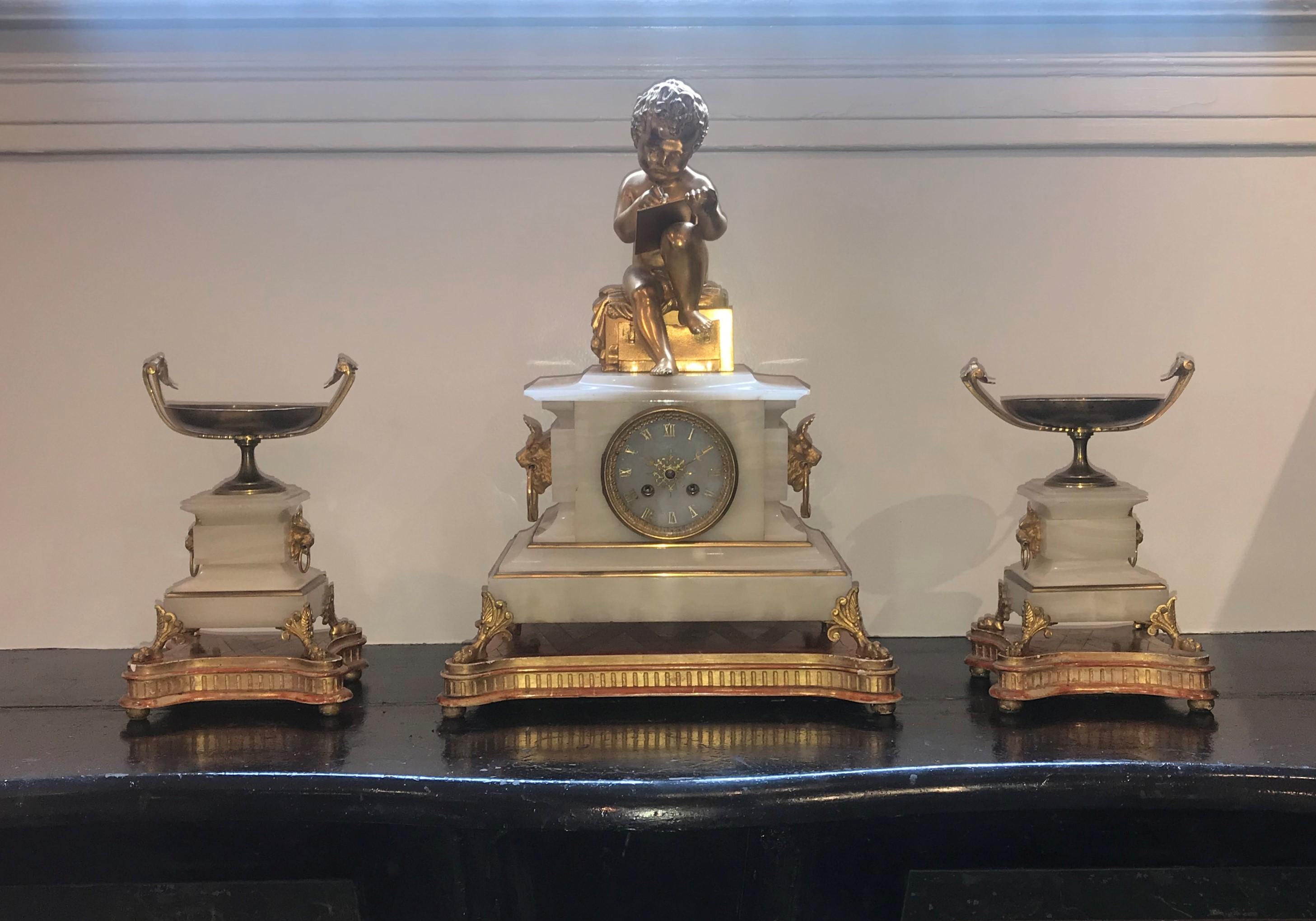 Mantel (fireplace) clock and pair of taza compotes. French white onyx and ormolu by Dasson and Godeau of Paris.

Mantel (fireplace) clock with ormolu boy writing on a tablet, bull heads with rings on either side. Perteme Marseille on dial.
18