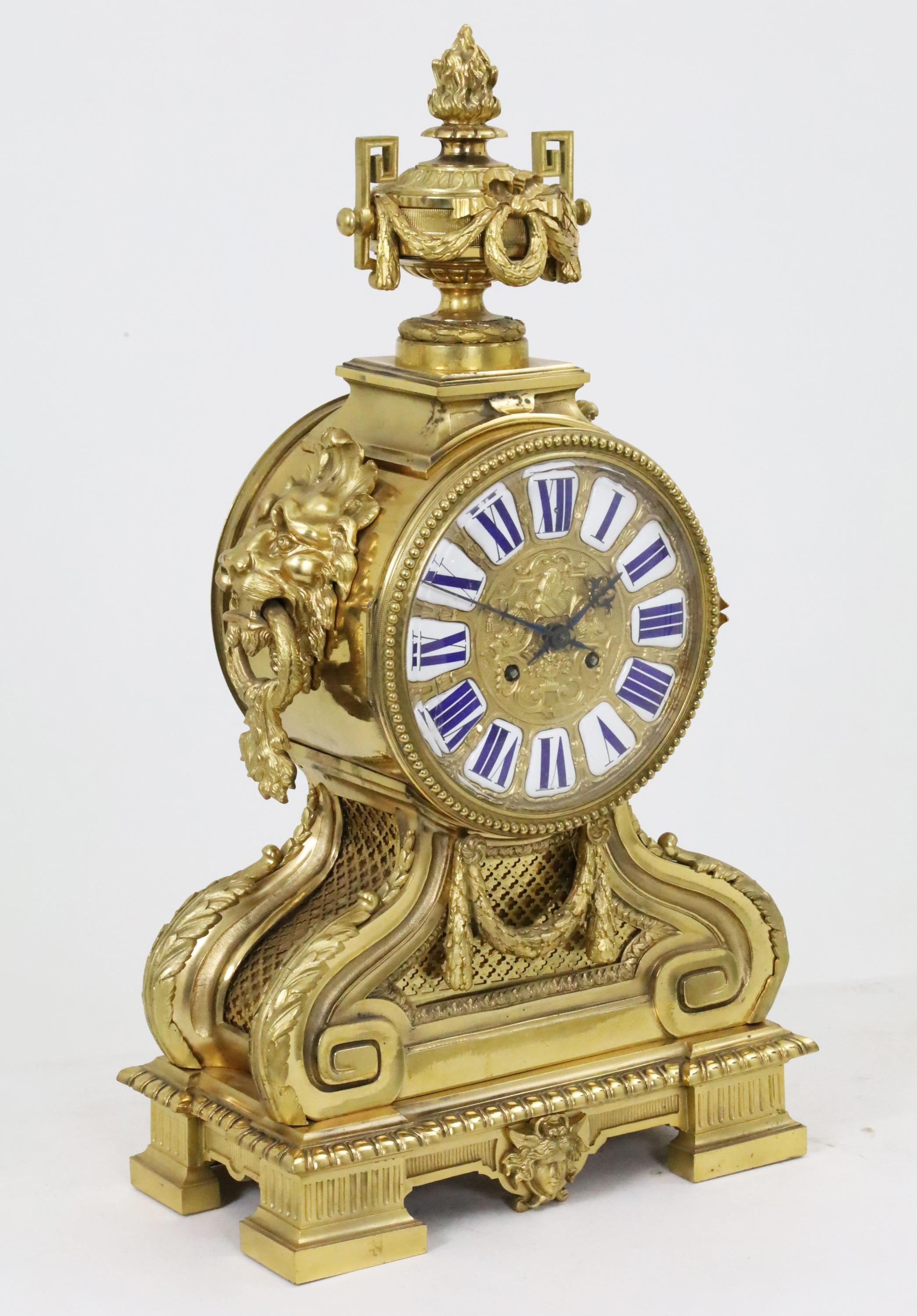 Set di orologi francesi in bronzo in tre pezzi con frontone a urna e a festoni e maniglie a testa di leone, quadrante in rilievo con numeri in porcellana incastonati, insieme a una coppia di candelabri a 9 luci conformi, XIX secolo