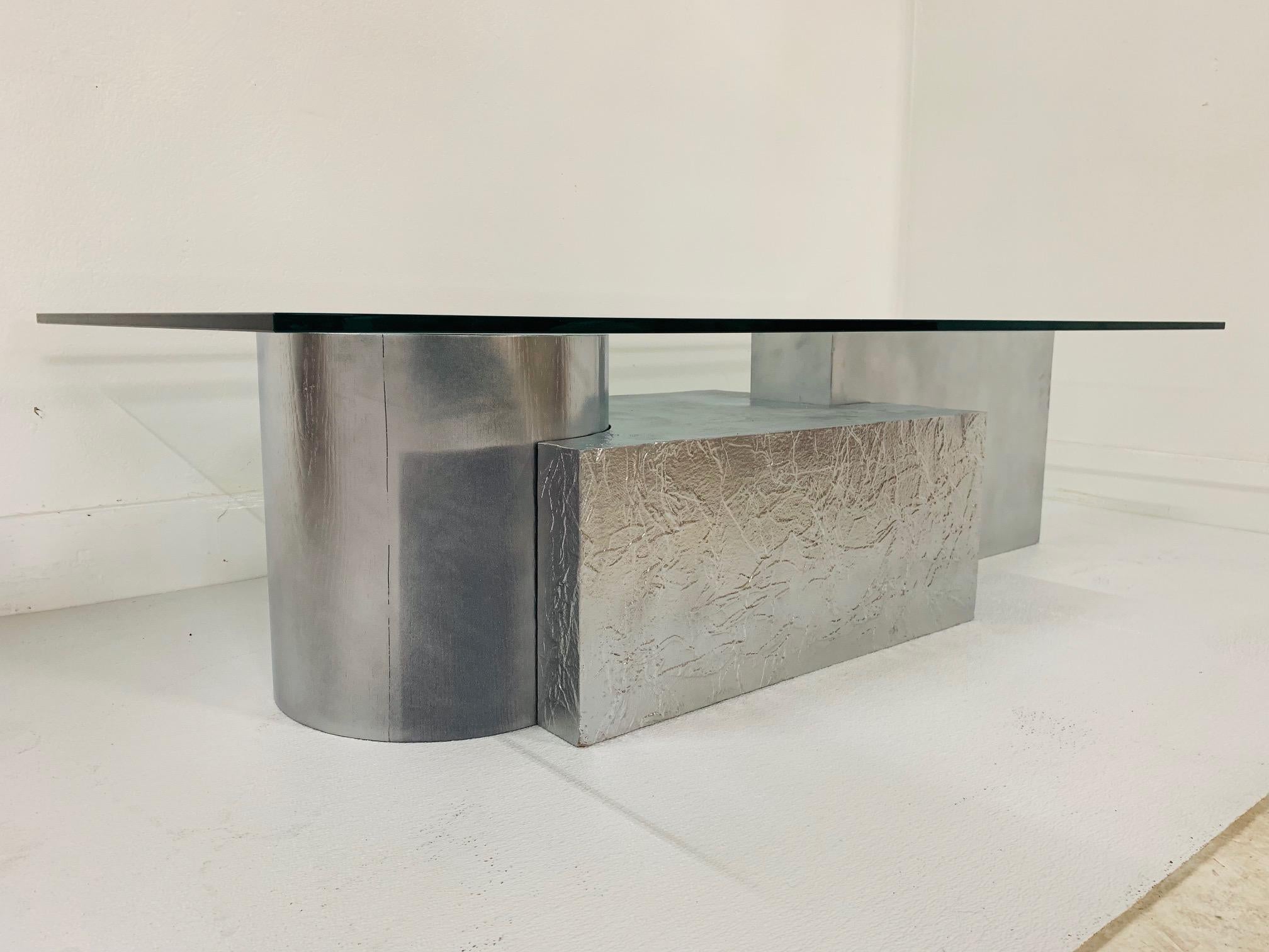 Three-piece geometrical coffee table. Unique base comprising of three sections which depicts 3-D puzzle pieces. Surfaces are textured and flat. Has the original glass. Each piece has a painted silver finish. Paul Evans style.