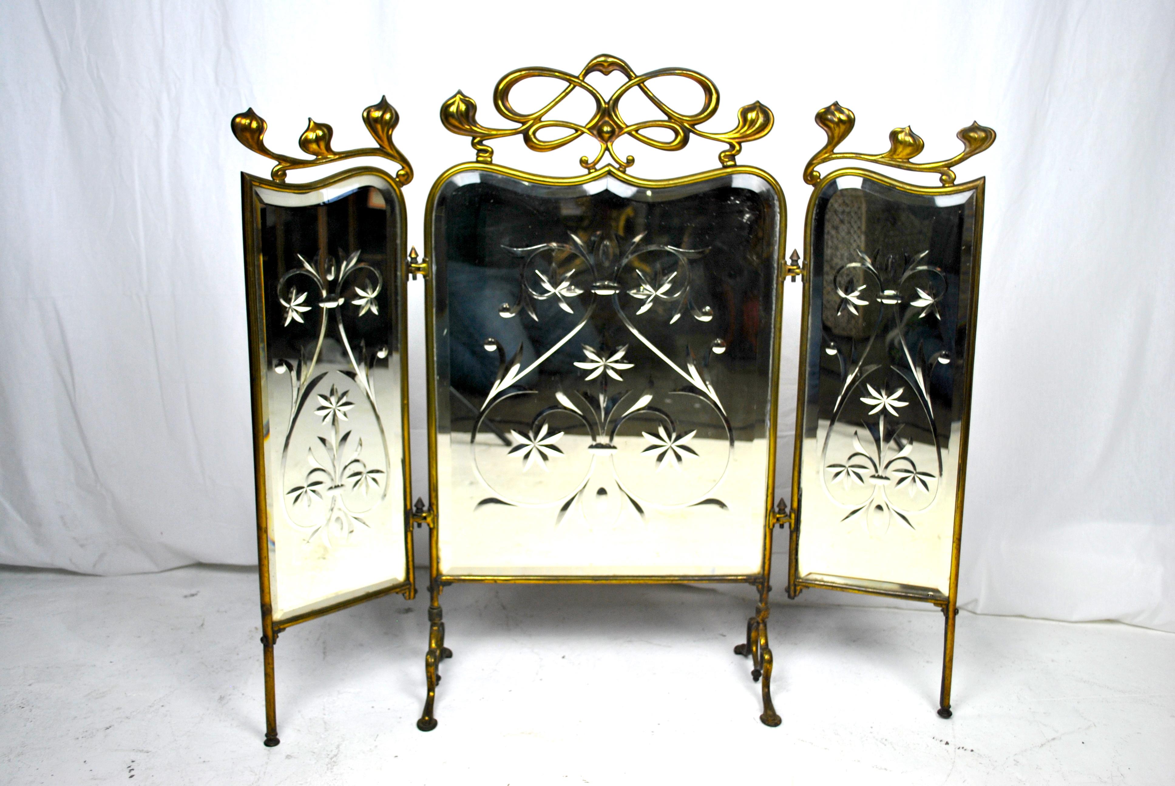 A beautiful and original Art Nouveau fire screen. A three-piece hinged mirrored Art nouveau fire fender screen. The screen has a highly stylized brass gold gilt frame that has Art Nouveau detailing, a flowing top handle and splayed feet. Each of the