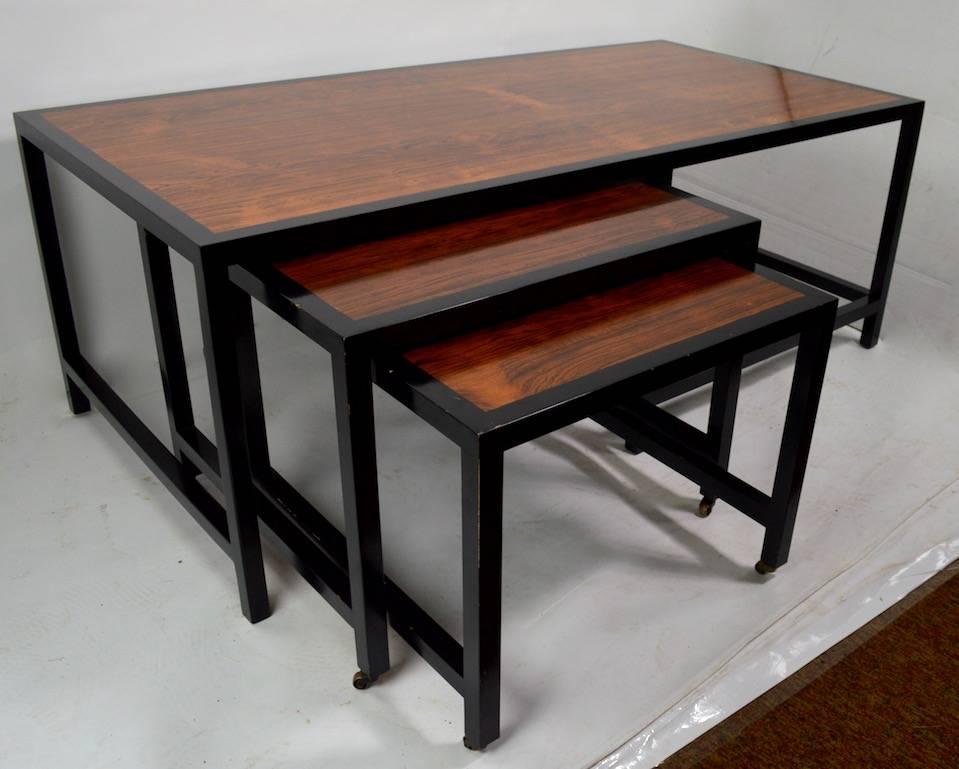 Architectural nesting tables design attributed to Probber. Stunning rosewood tops with black ebonized trim frame. Larger rectangular table accepts two smaller square tables, smaller tables have brass wheels. Tables show some very minor cosmetic