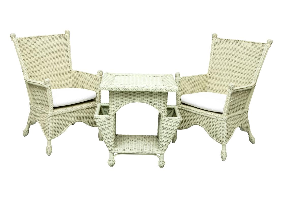 A well made, comfortable and colorful three piece wicker Porch Set consisting of two Armchairs in  Sage Green paint with white cotton seats along with a wicker table featuring a flat top, a lower shelf, and two open compartments on the sides that