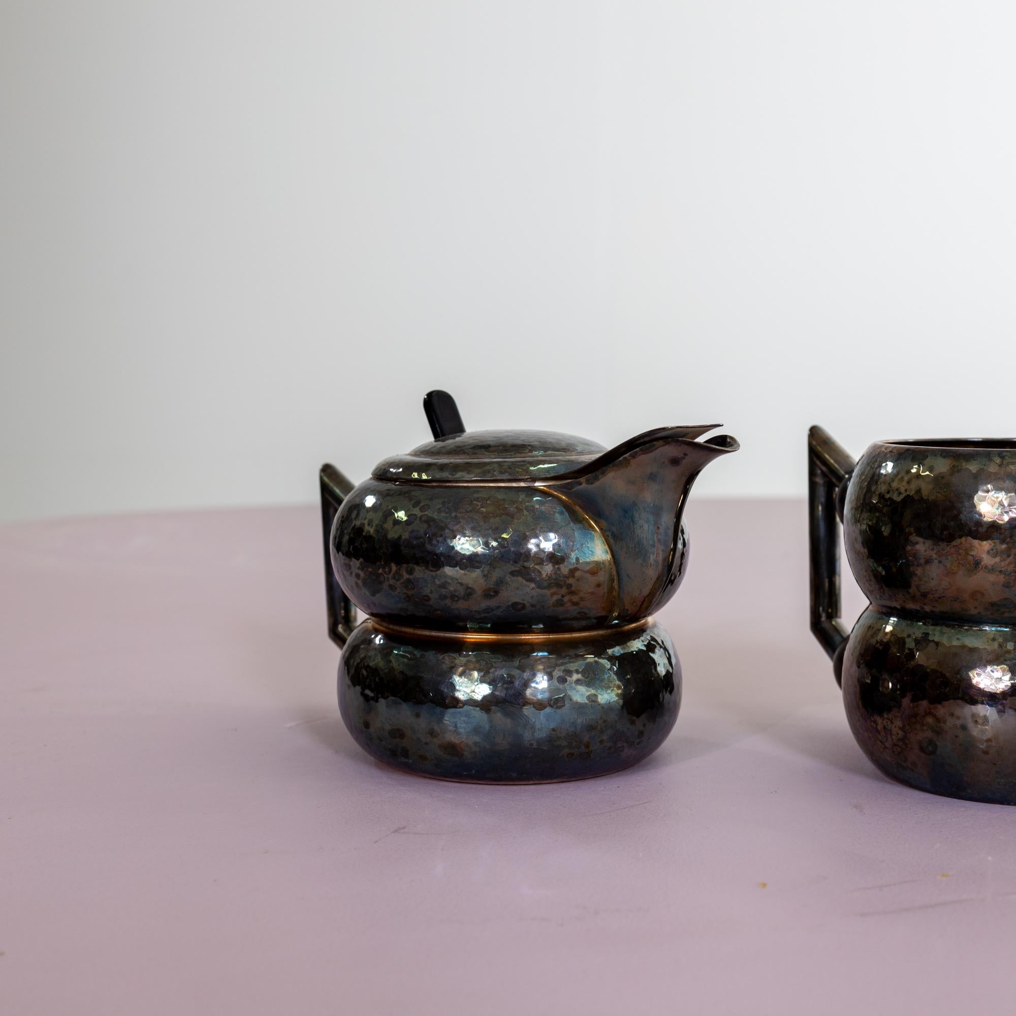 Decorative tea set consisting of a teapot, a milk jug and a coffee pot in double-bellied shape and textured wall. The acute-angled handles are connected to the body via black wooden beads, which insulates the handle from the heat.