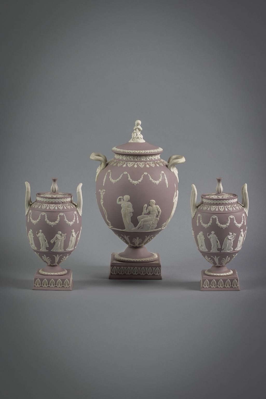 Lilac ground. Each encircled by frieze of classical figures beneath floral swags, the largest flanked by serpent handles with mask terminal and Cupid finial, impressed WEDGWOOD, MADE IN ENGLAND, the smaller pair with upright reeded handles and bud
