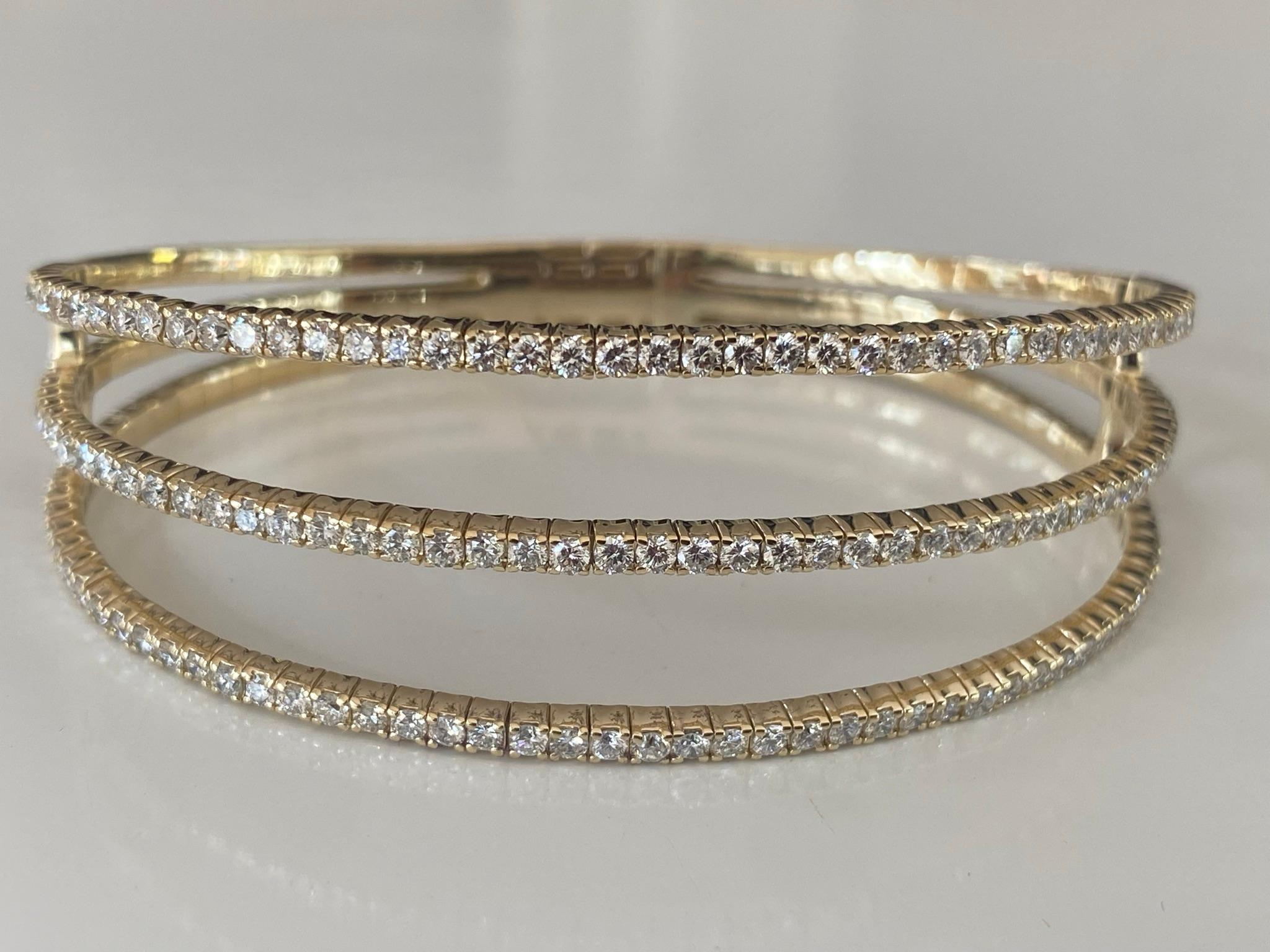 Crafted from 14kt yellow gold, this flexible bangle bracelet features 141 round diamonds, G color, VS-SI clarity that glisten over three rows. The diamonds total 3.47 carats and the bracelet measures 7 inches. 
